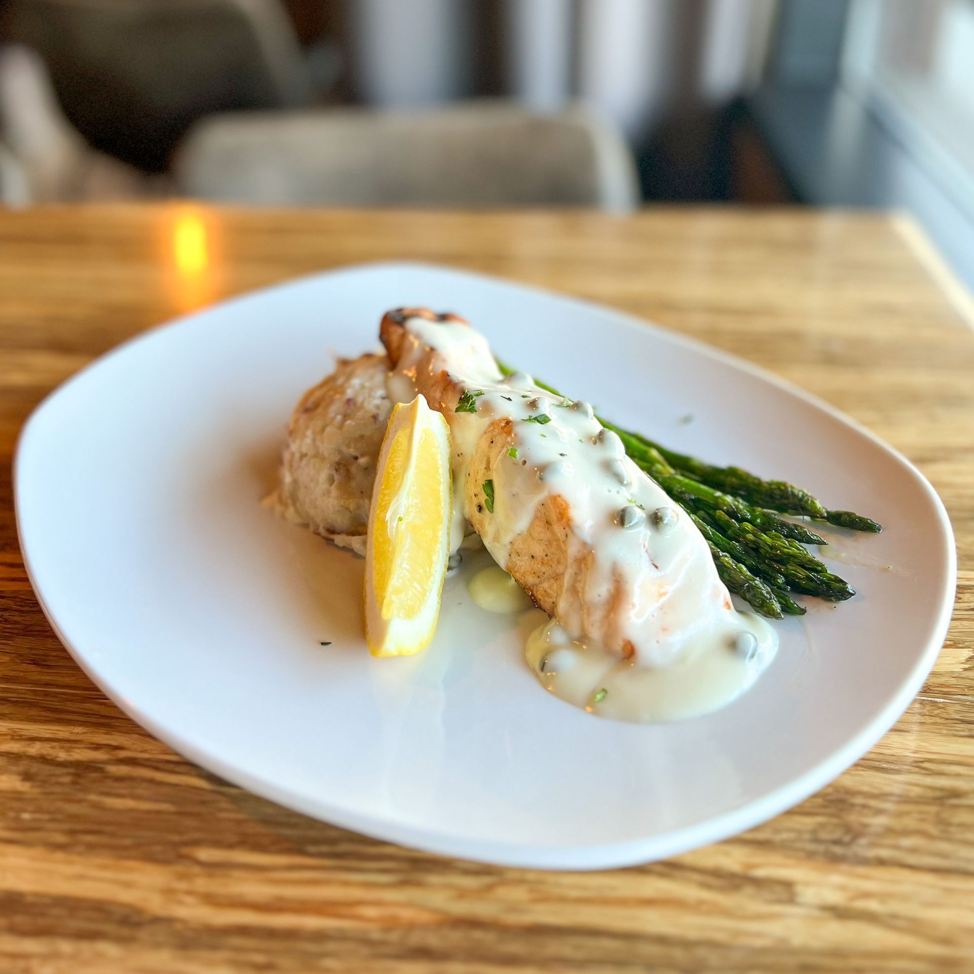 Plated Salmon with lemon butter caper sauce. Served on top of grilled asparagus, garlic mashed potatoes, and a lemon wedge. 
