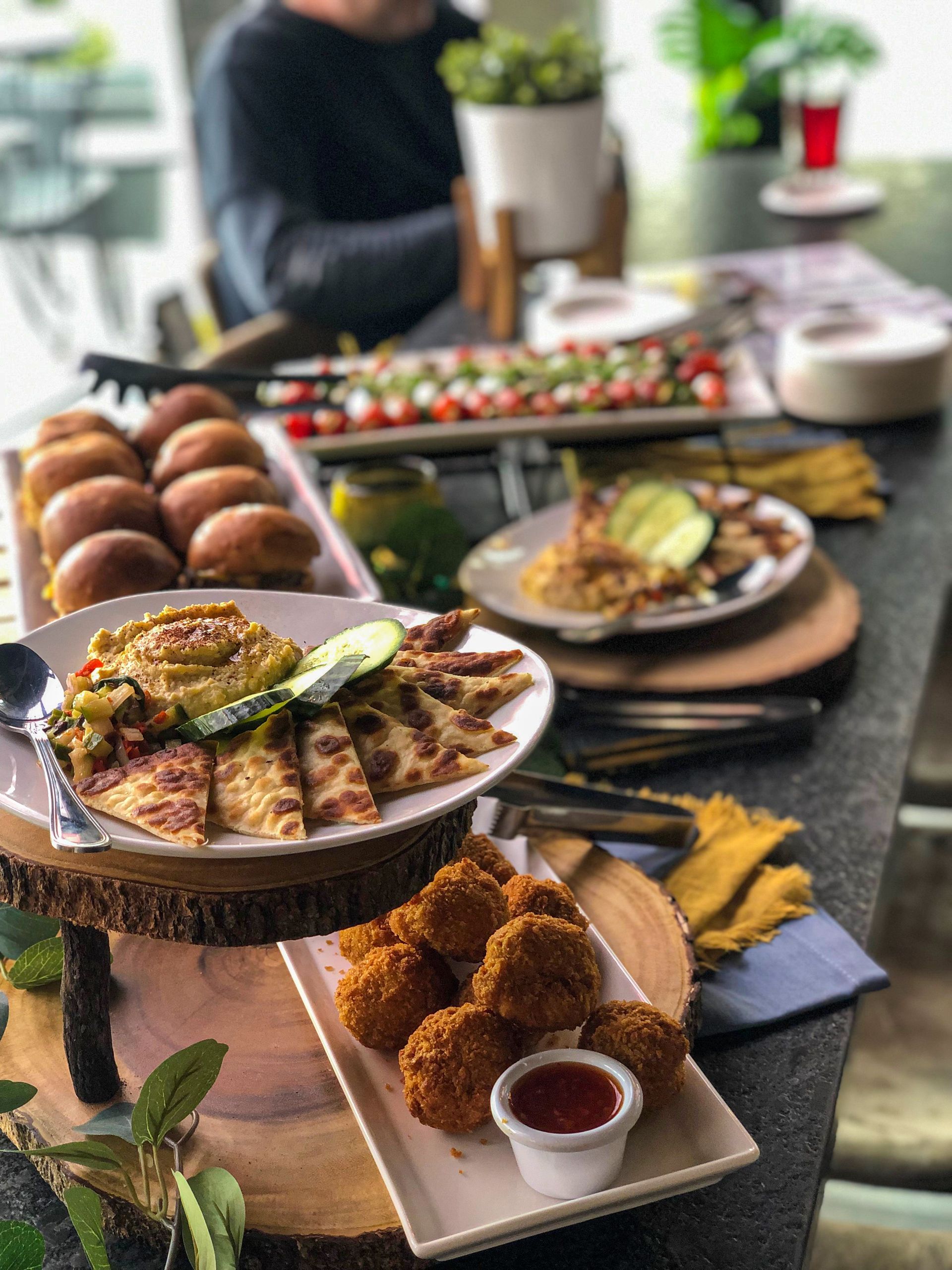 Assortment of appetizers plated on a buffet table. Quesadillas, mac & cheese balls, and sliders can be seen. 
