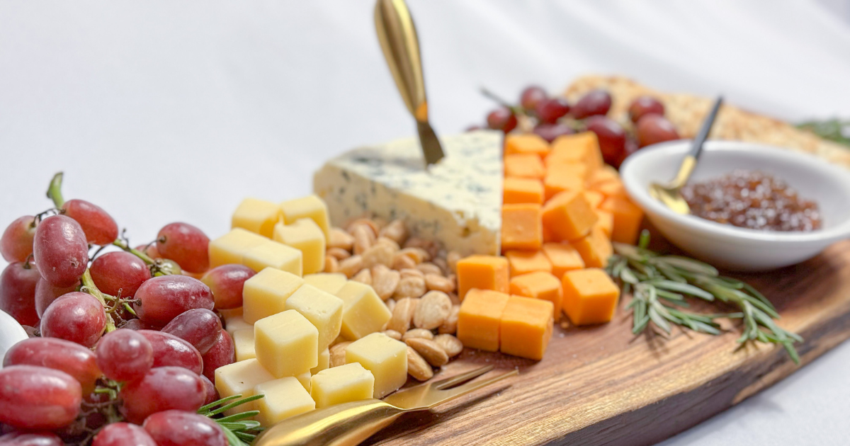 Charcuterie platter with cubed cheeses, a triangle of blue cheese with a gold cheese knife in it, grapes, and marcona almonds. 