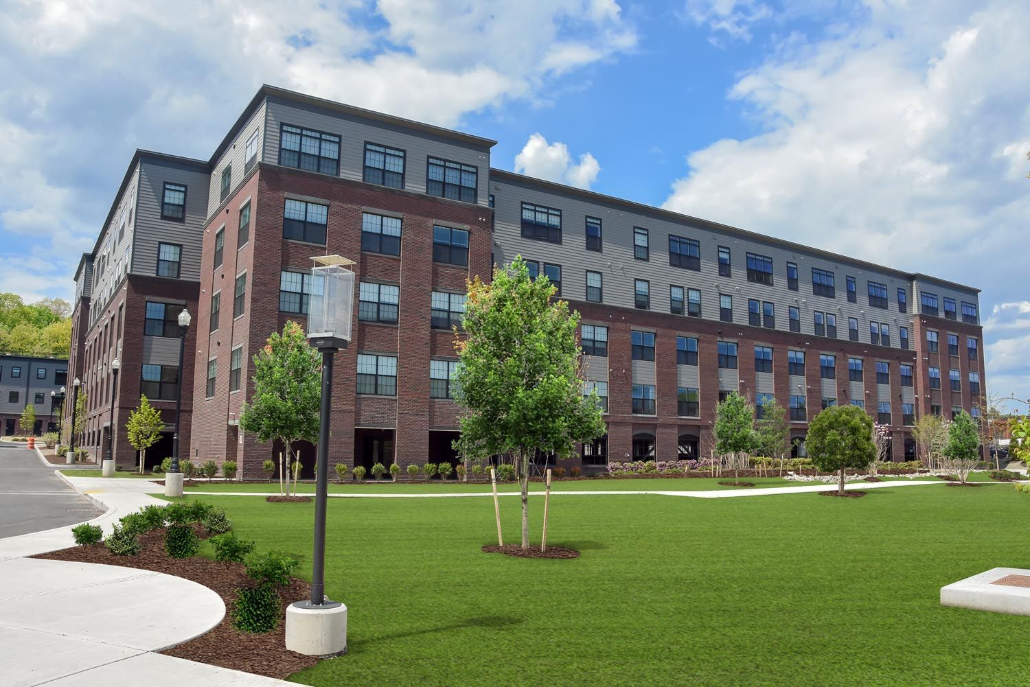A large brick building with a lot of windows is surrounded by trees and grass.