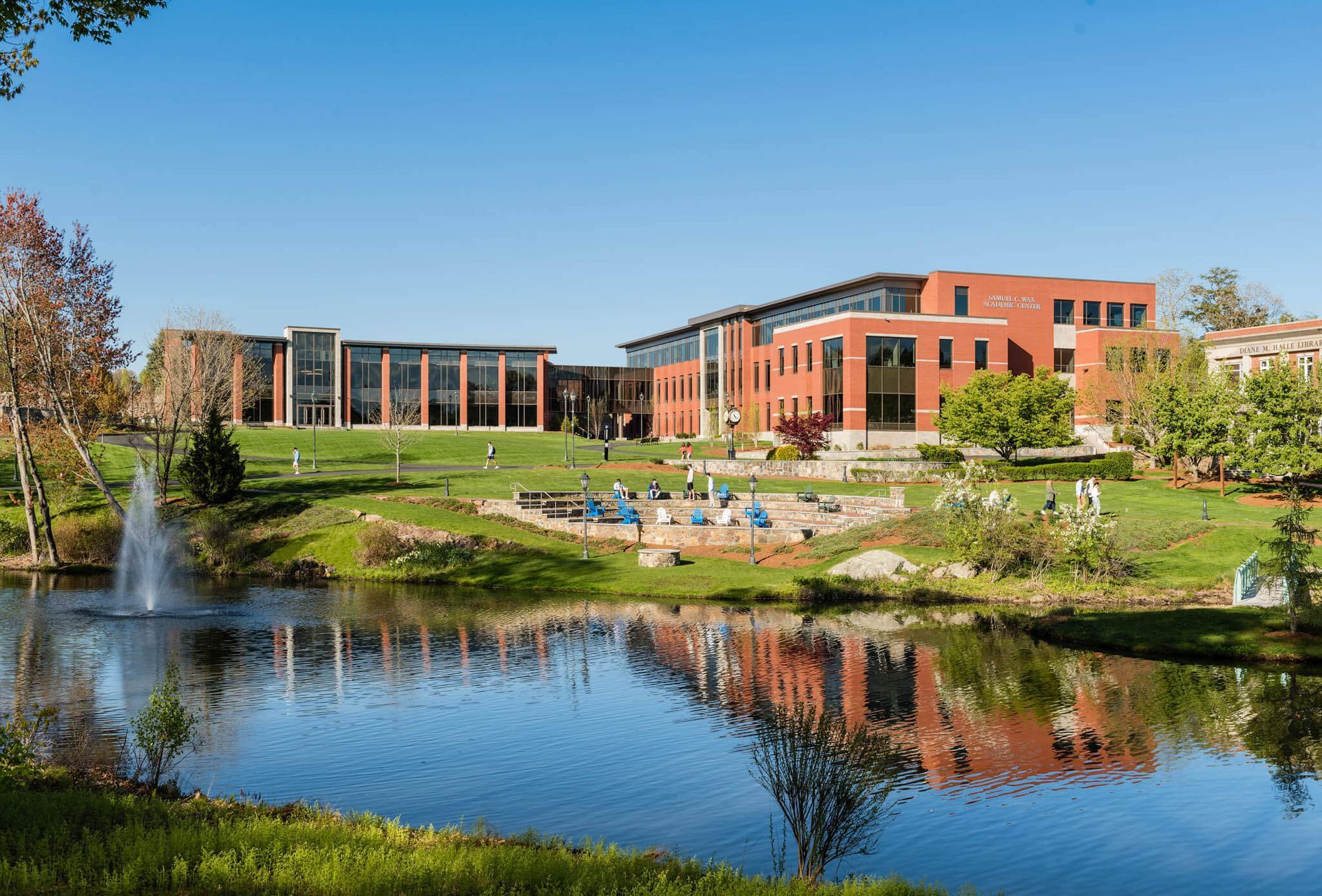 A large building with a fountain in front of it is reflected in a pond.