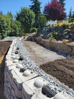 A stone wall is being built next to a dirt road.