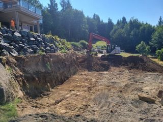 A large excavator is digging a hole in the dirt in front of a house.