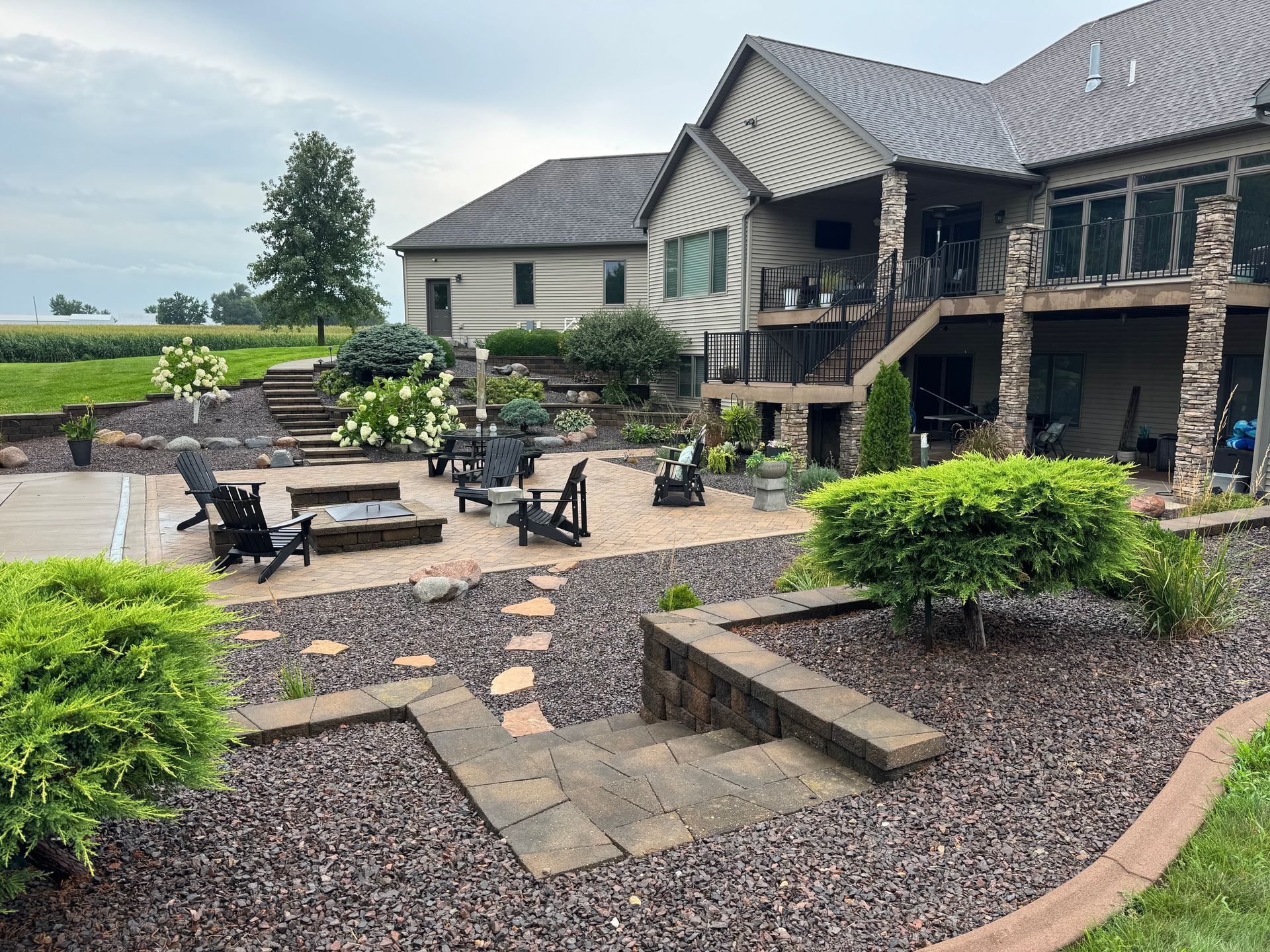 Custom paver patio and fire pit with retaining walls, stone steps, and landscaped garden beds in New London, Iowa.