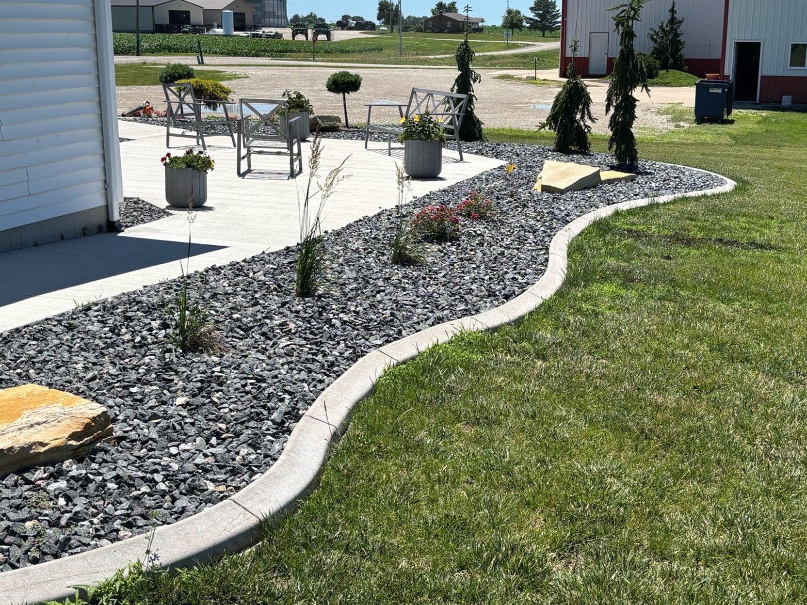 Curved rock garden border with small shrubs beside a green lawn and patio seating outdoors