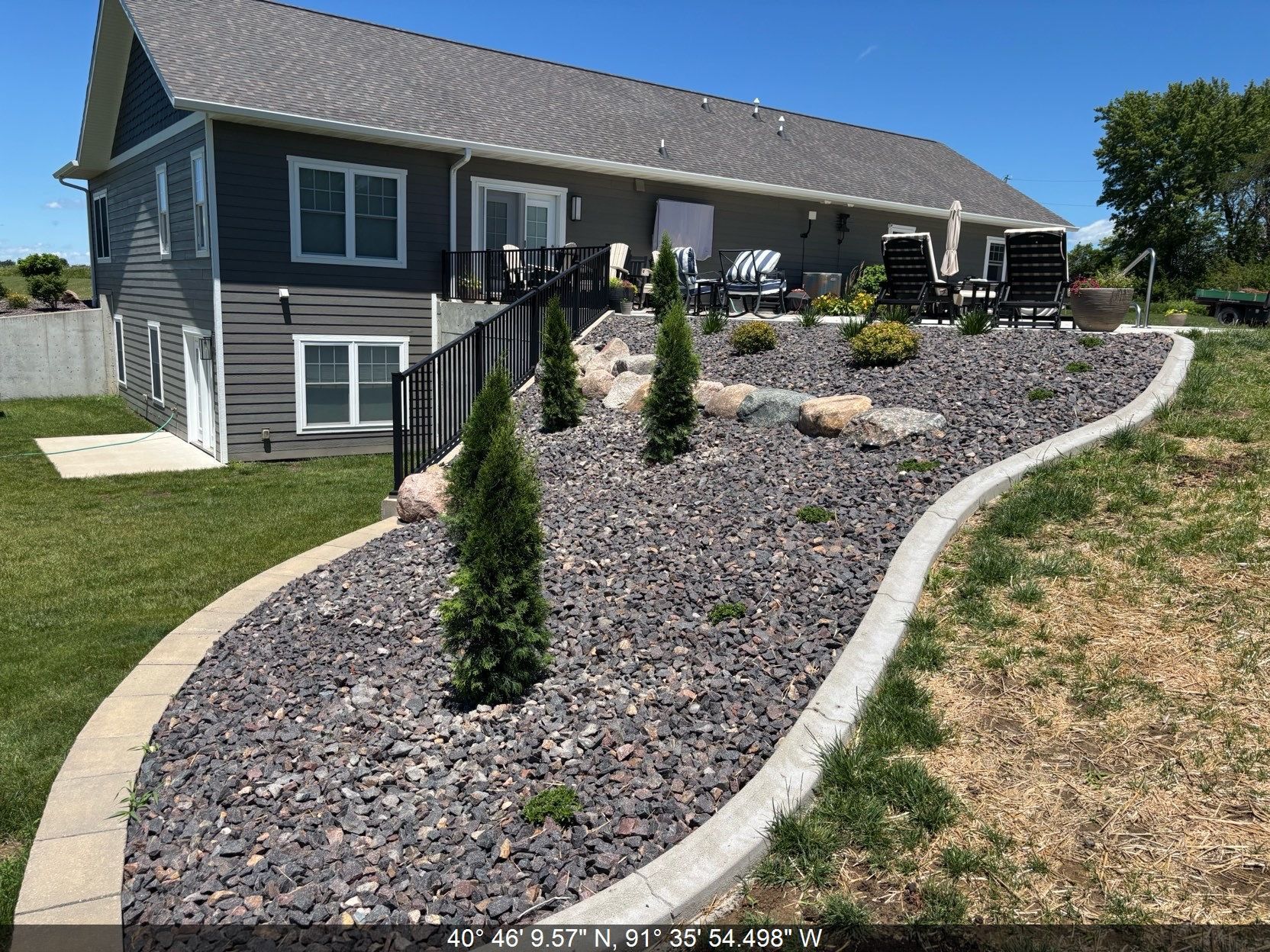 Gray two-story house with stone landscaping and a sloped gravel garden under a blue sky