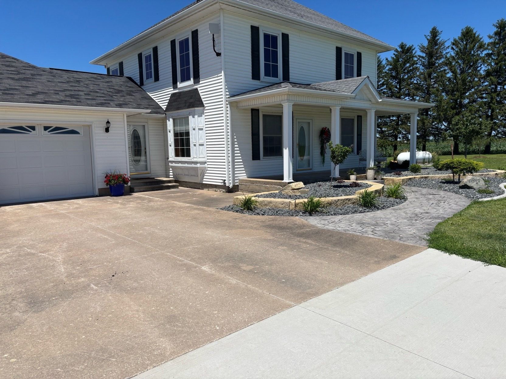 White two-story house with attached garage, driveway, and front porch in a sunny suburban setting