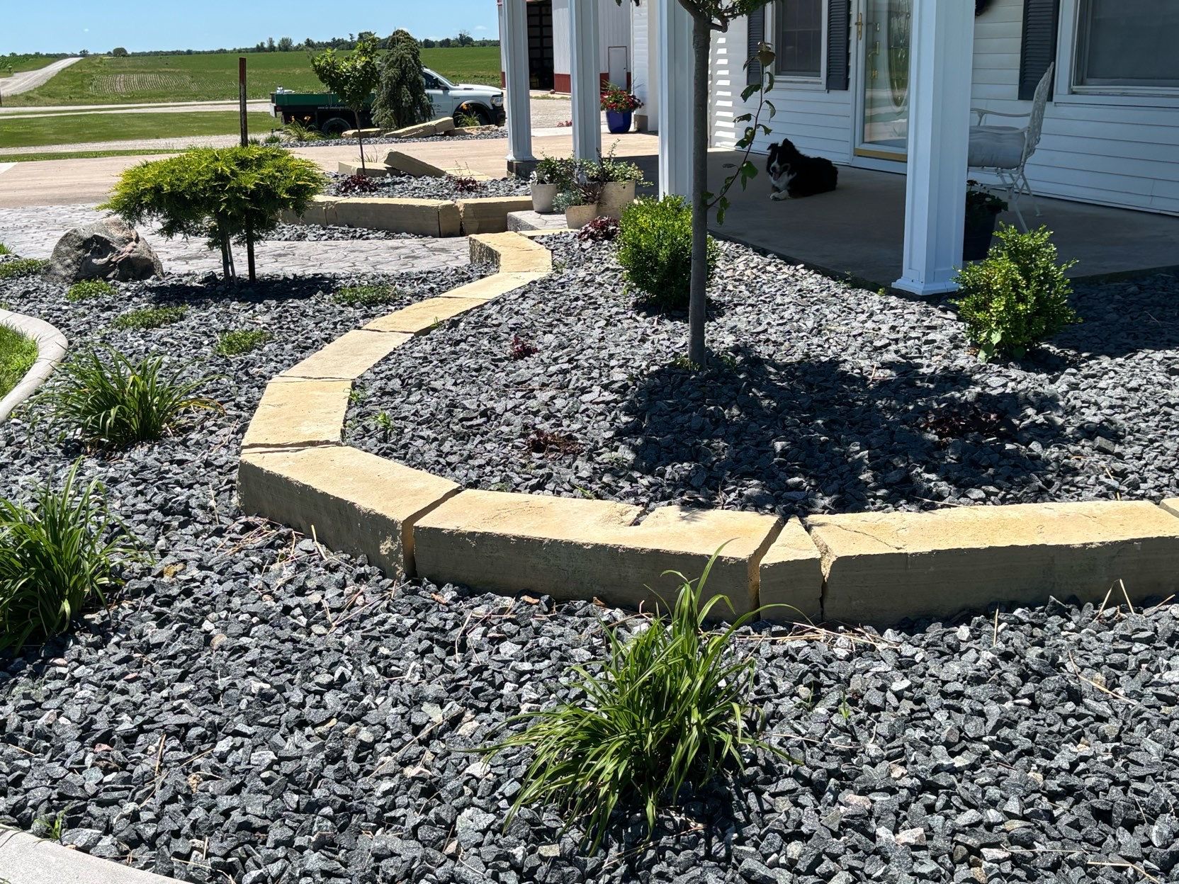 Landscape bed with gray rocks, yellow edging, and small shrubs beside a house.
