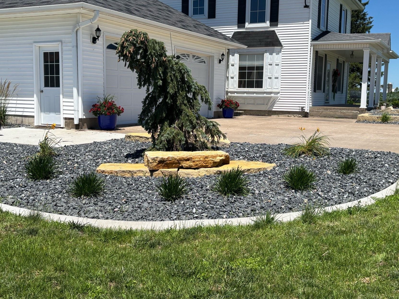 Front yard landscape with a curved gravel bed, small tree, and a white house in the background