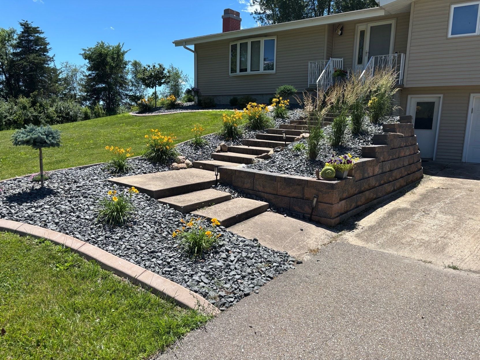 Front yard terraced stone steps with gravel landscaping beside a beige house and driveway