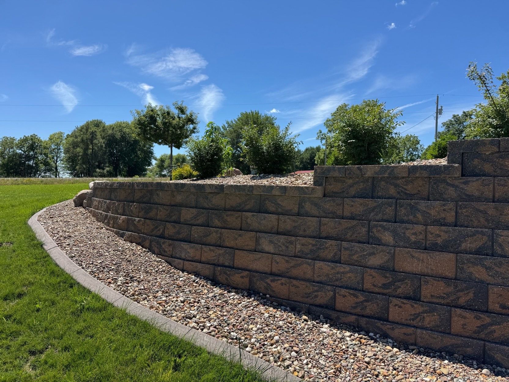 Curved stone retaining wall along a landscaped grassy slope under a blue sky