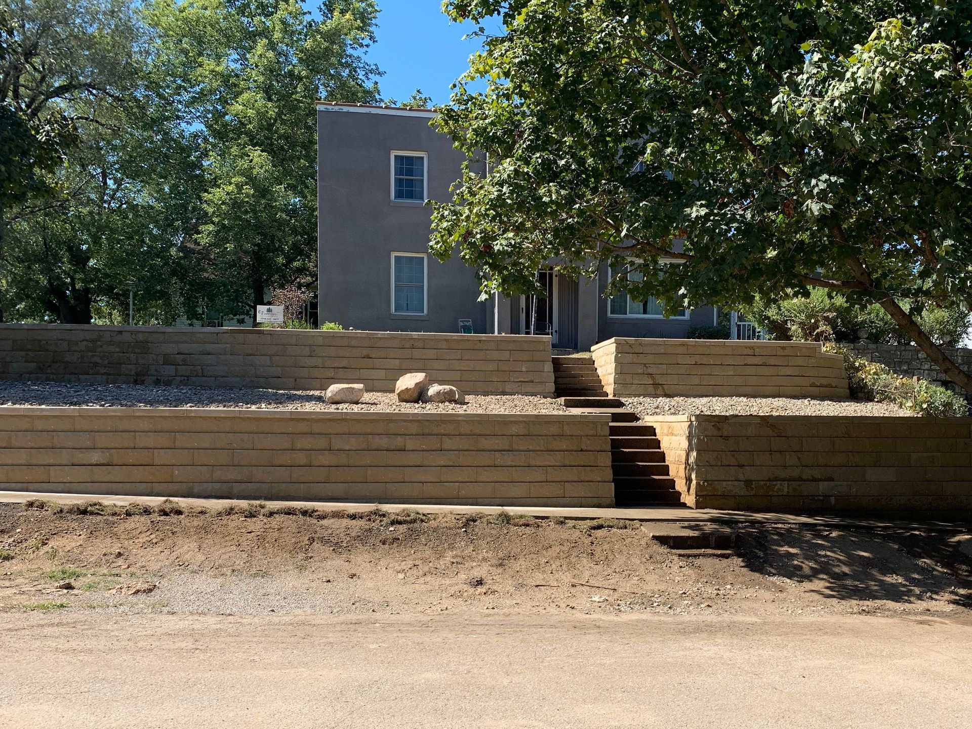 Terraced steps leading up to a gray house under trees on a sunny day