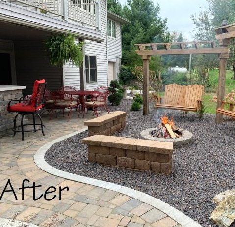 Backyard patio with fire pit, wood swing, red chairs, and stone seating beside a house
