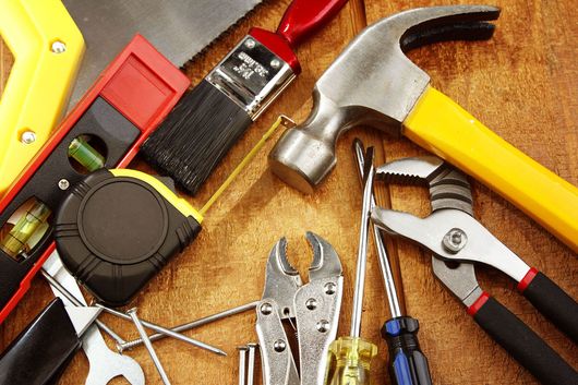 Assorted hand tools on a workbench, including a hammer, pliers, screwdriver, tape measure, and utility knife