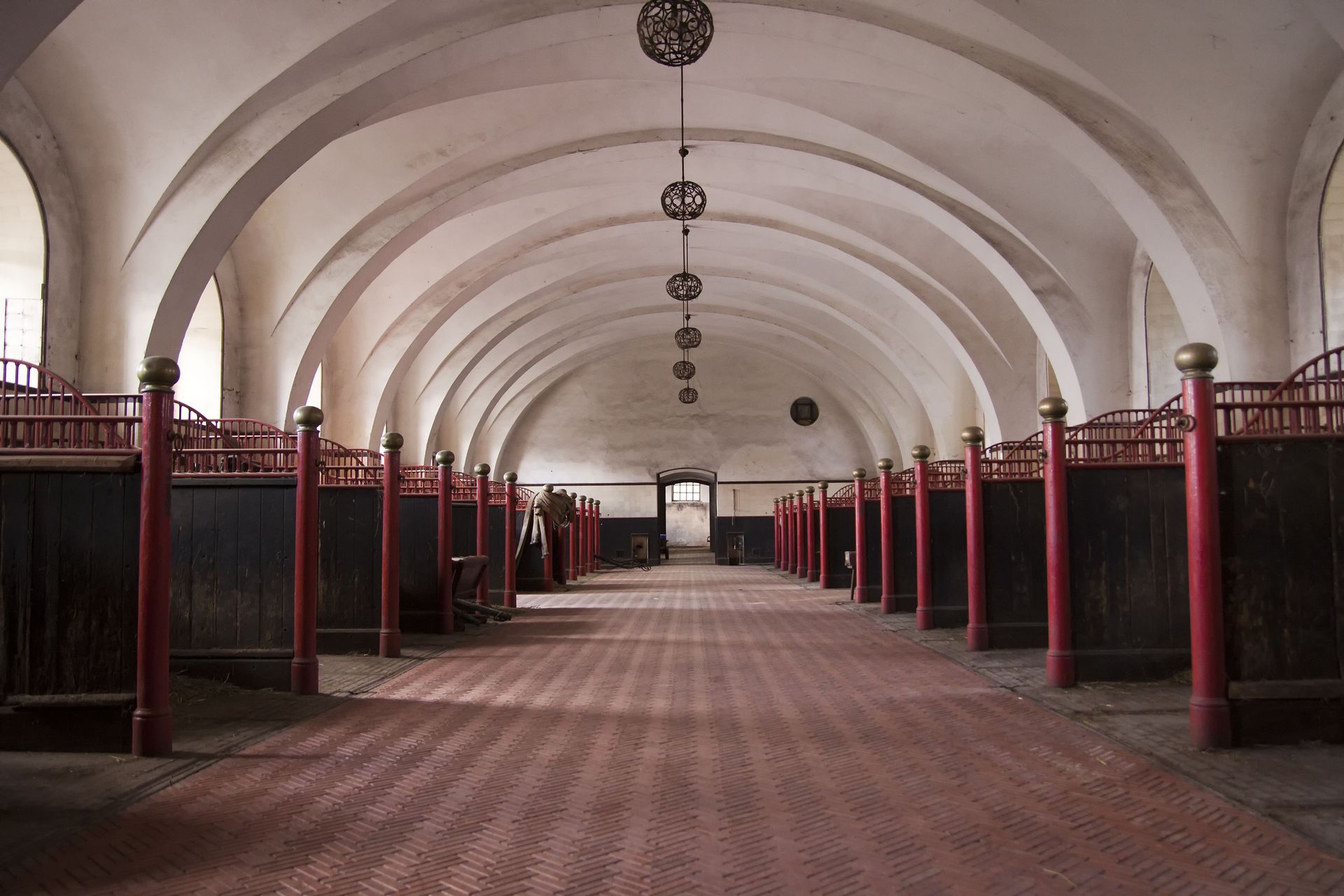 Empty arched hall with red posts, brick floor, and hanging lights