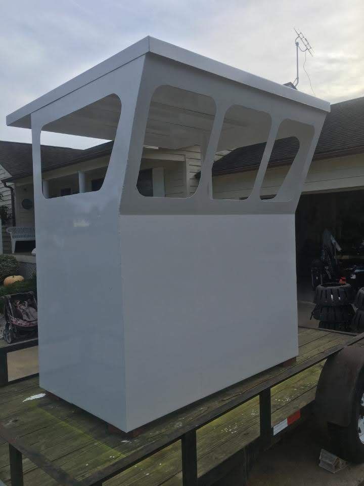 Gray metal structure resembling a boat's cabin, set on a trailer. Features open windows and a flat roof.