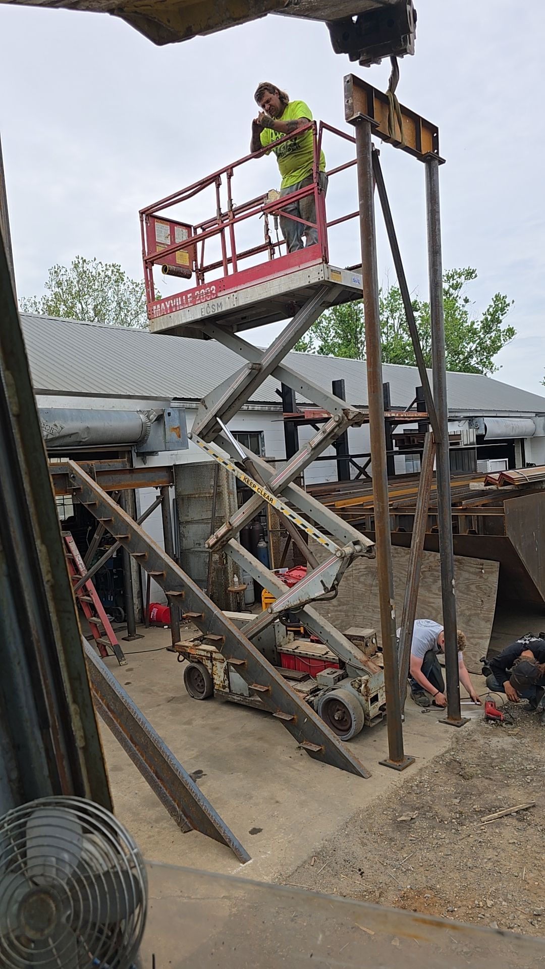 Worker on a lift welding metal beams outdoors.  Gray sky and industrial setting.