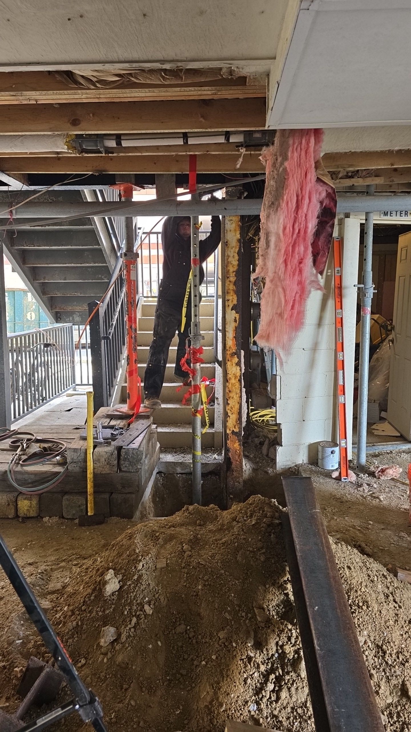 Construction site with worker on stairs. Support jacks hold ceiling. Debris and dirt in foreground.
