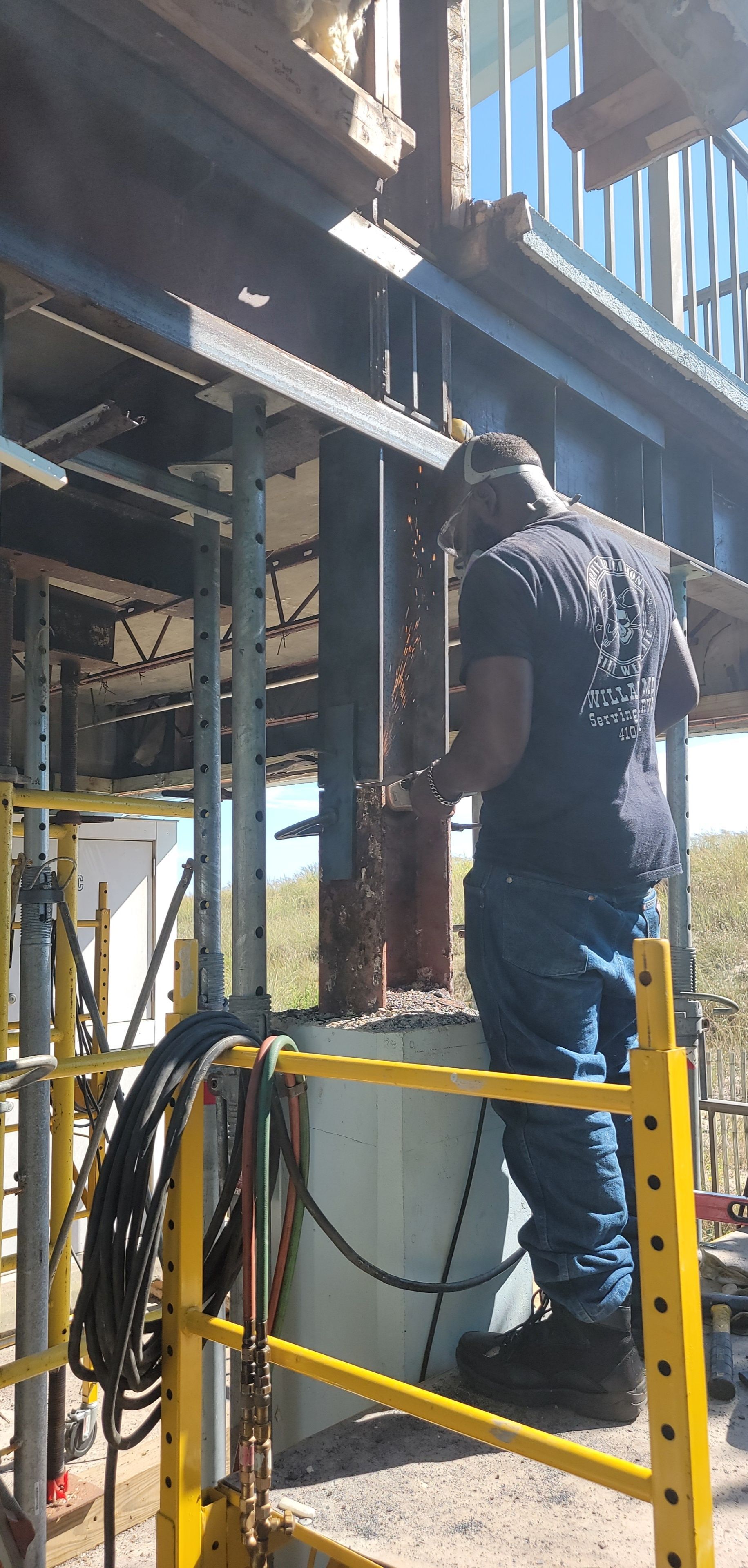 Construction worker using a torch on a metal beam while standing on a yellow scaffolding.