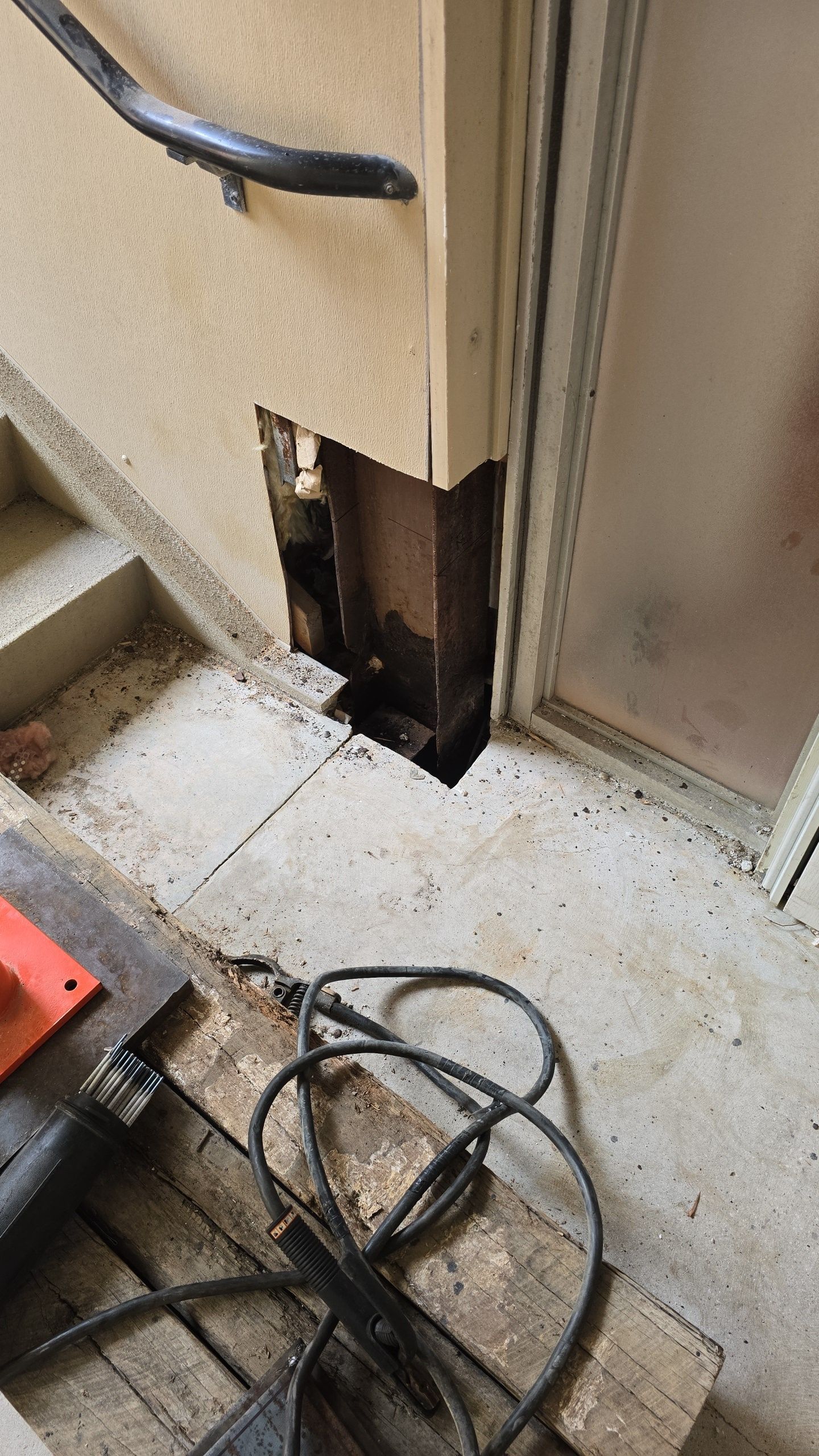 Damaged wall near stairs with exposed wood and construction tools.
