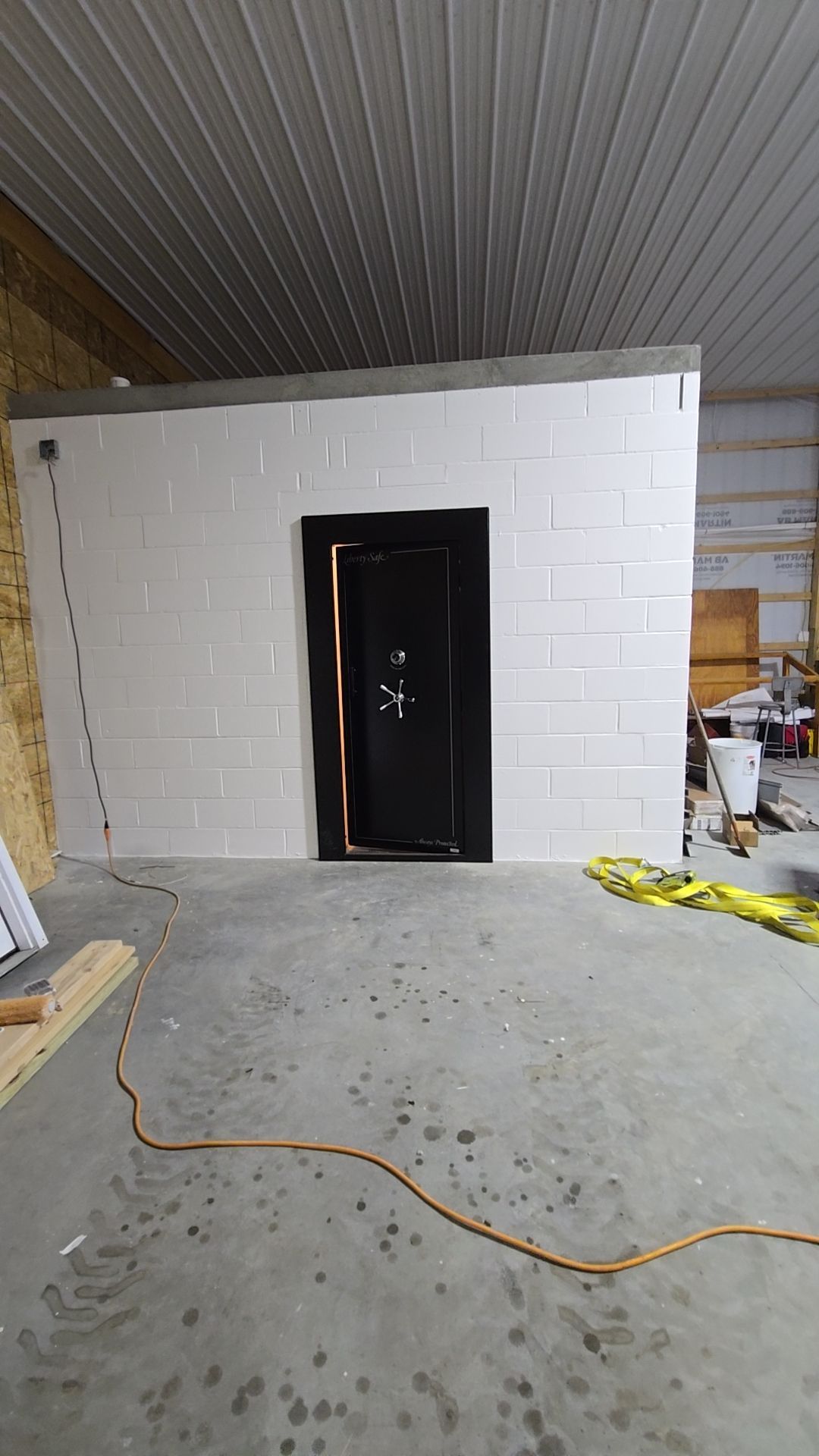 Black door set in white block wall, inside a workshop. Orange cord on floor.