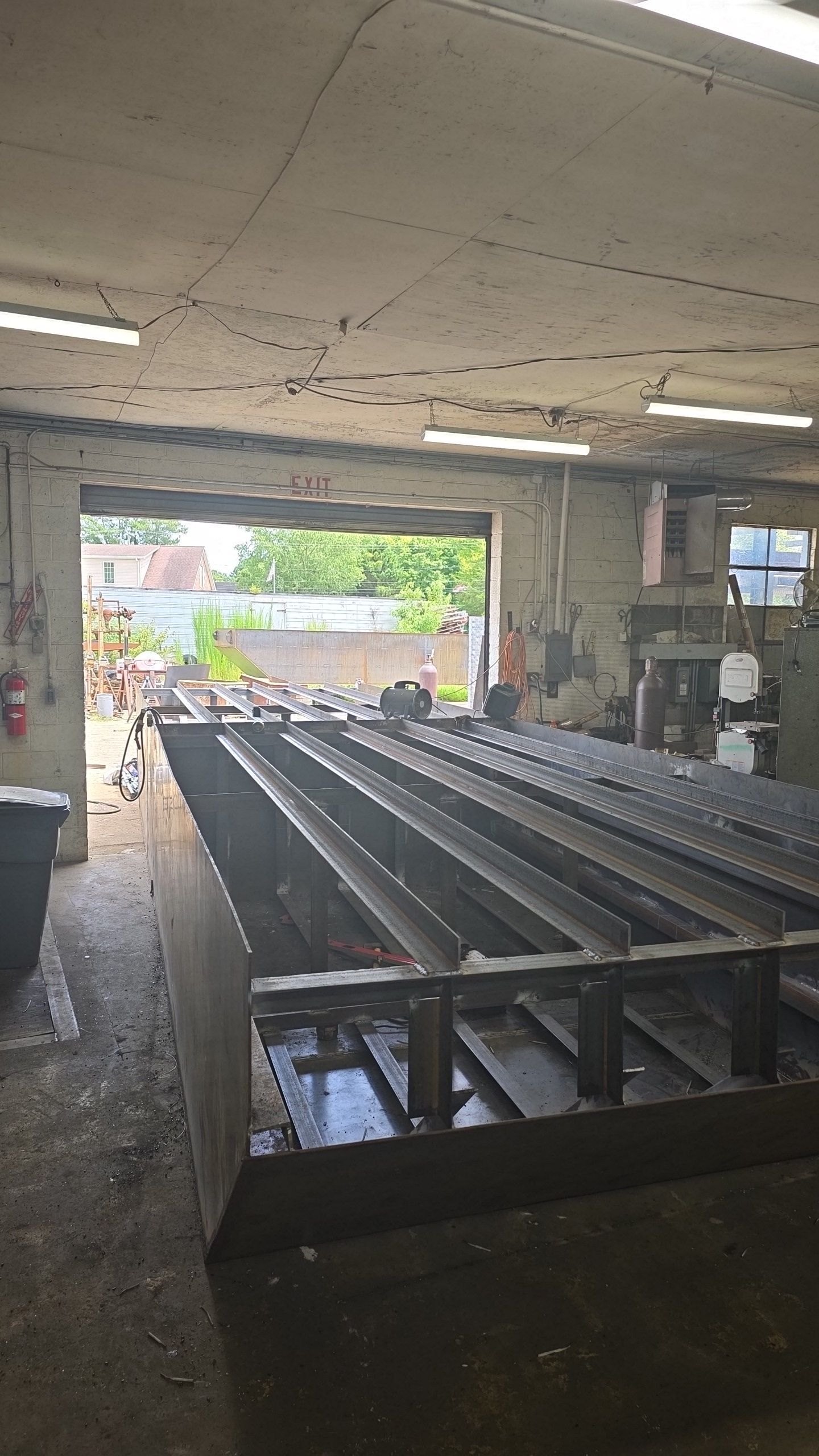 Metal fabrication shop with large steel frame in foreground, open doorway.