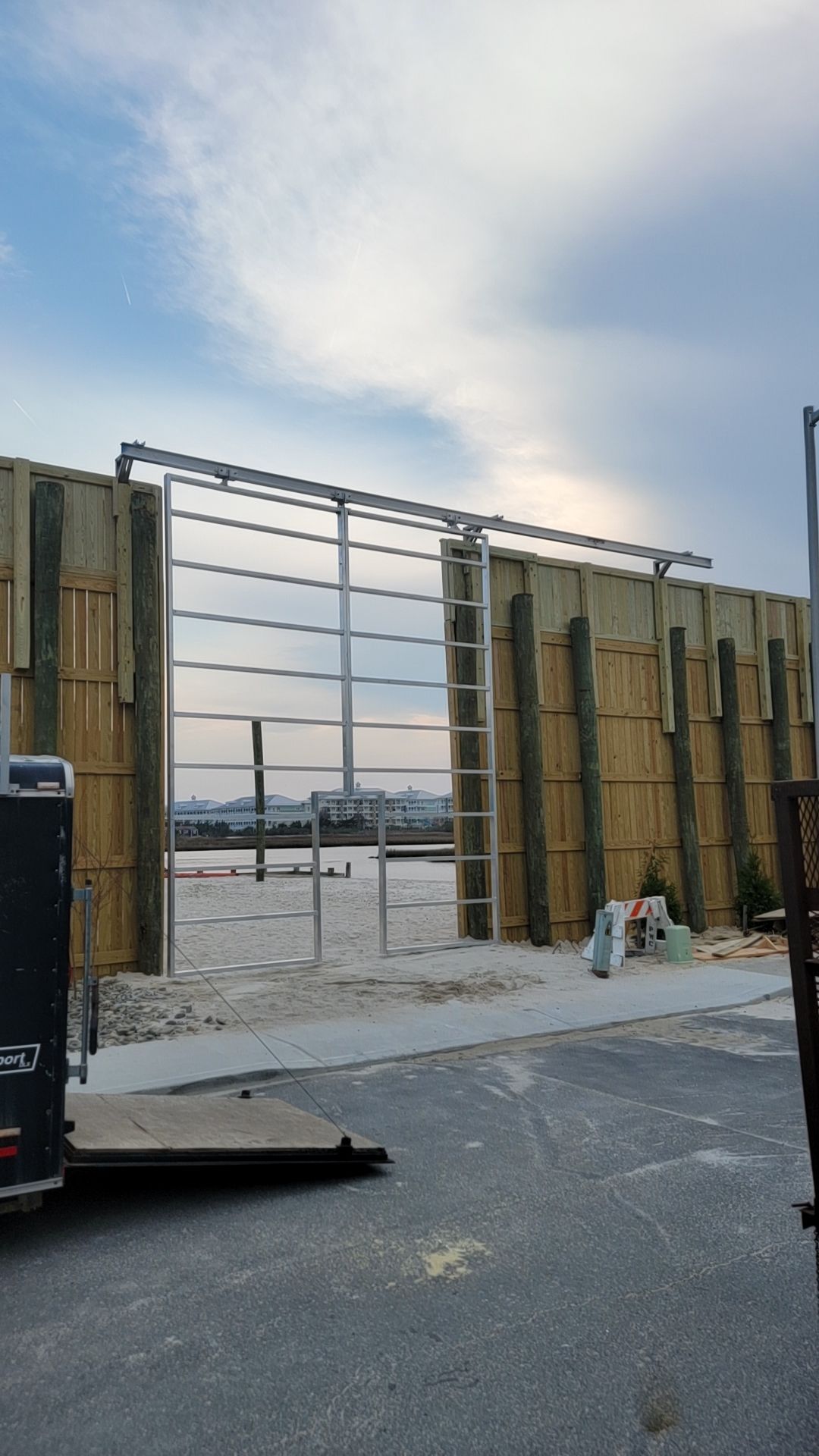 Metal sliding gate with ladder on wooden wall under a cloudy sky.