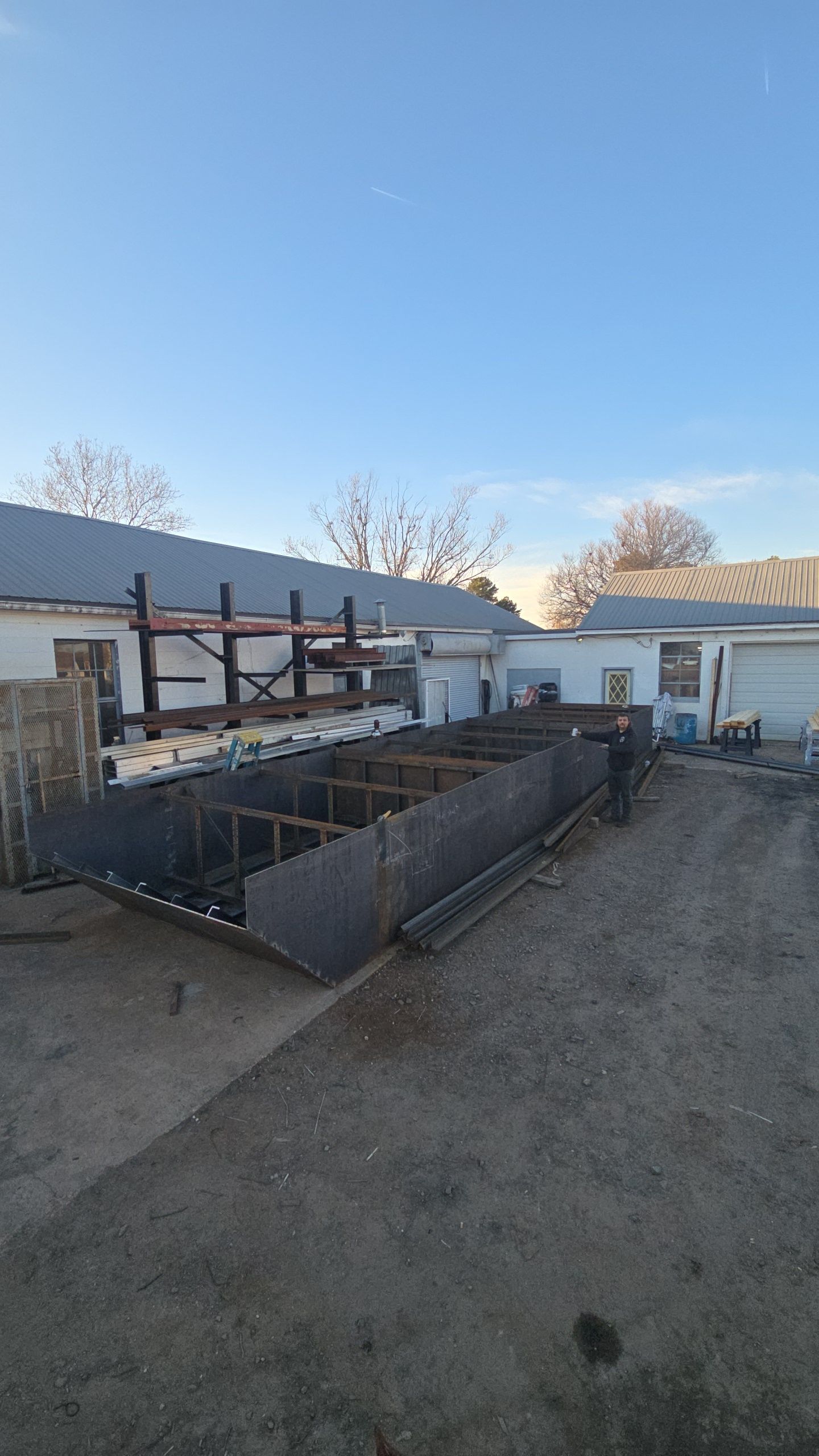 Steel forms on a gravel lot near white buildings under a blue sky.