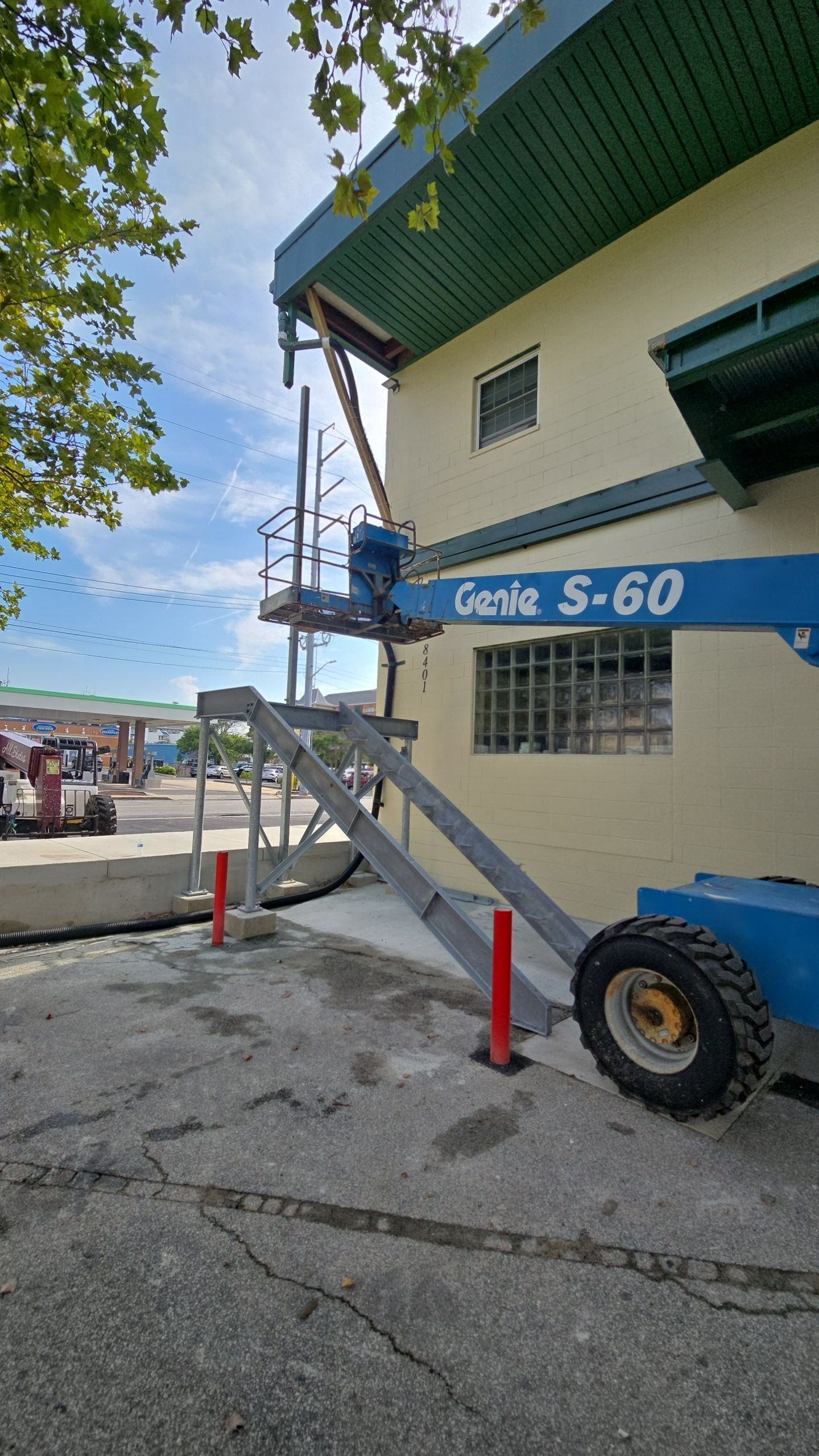 Blue Genie S-60 lift beside a light yellow building; red posts and concrete ground.