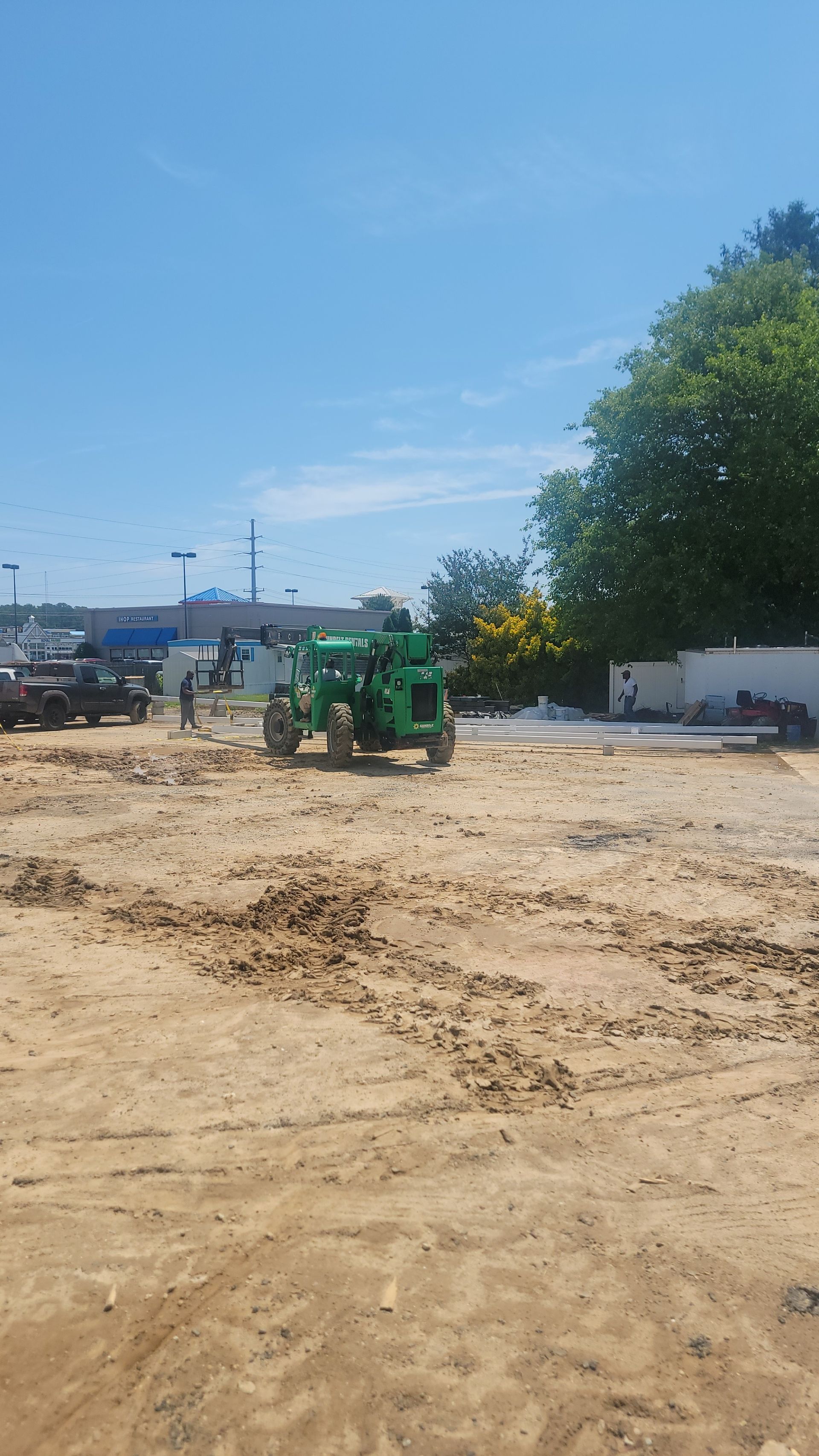 Construction site with green machinery, dirt, blue sky, and a glimpse of buildings.