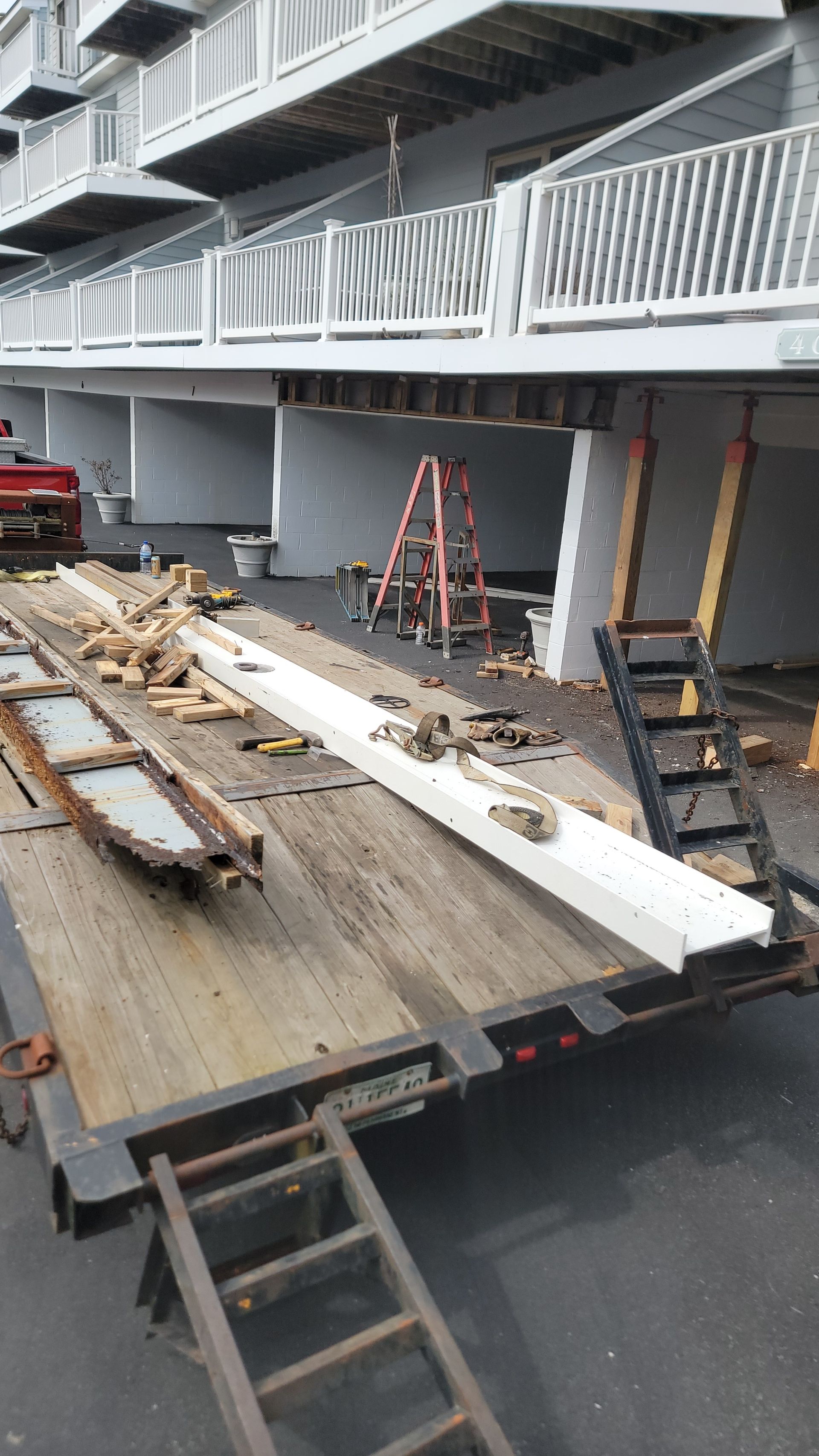 Trailer loaded with wood and construction materials beneath a building undergoing repairs.