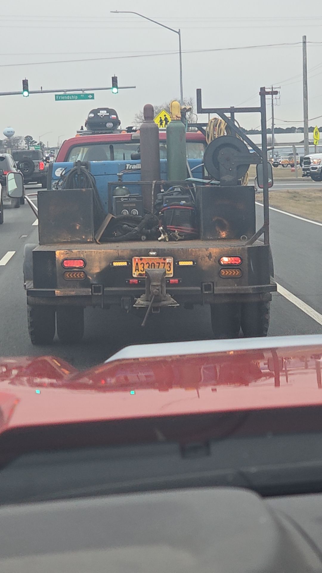 Welding truck on highway, equipment visible on flatbed. Tail lights, license plate, and hitch are present.