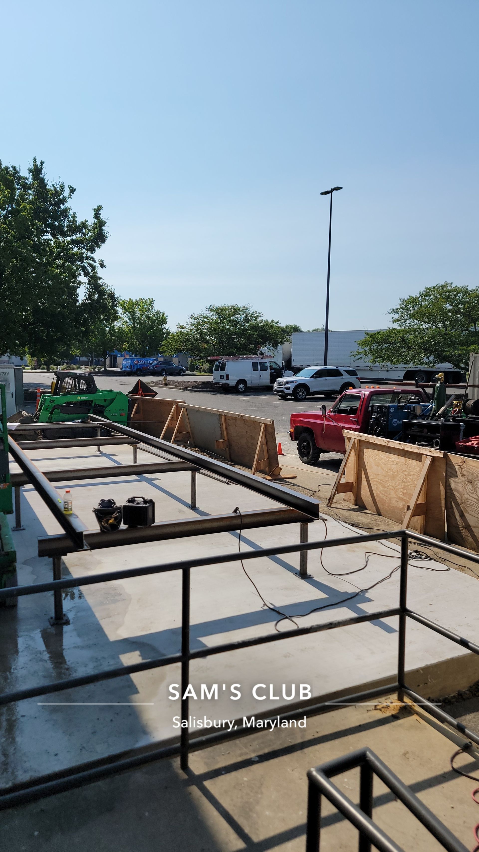Construction site at Sam's Club, metal frame, concrete, wooden barriers, vehicles, clear sky.