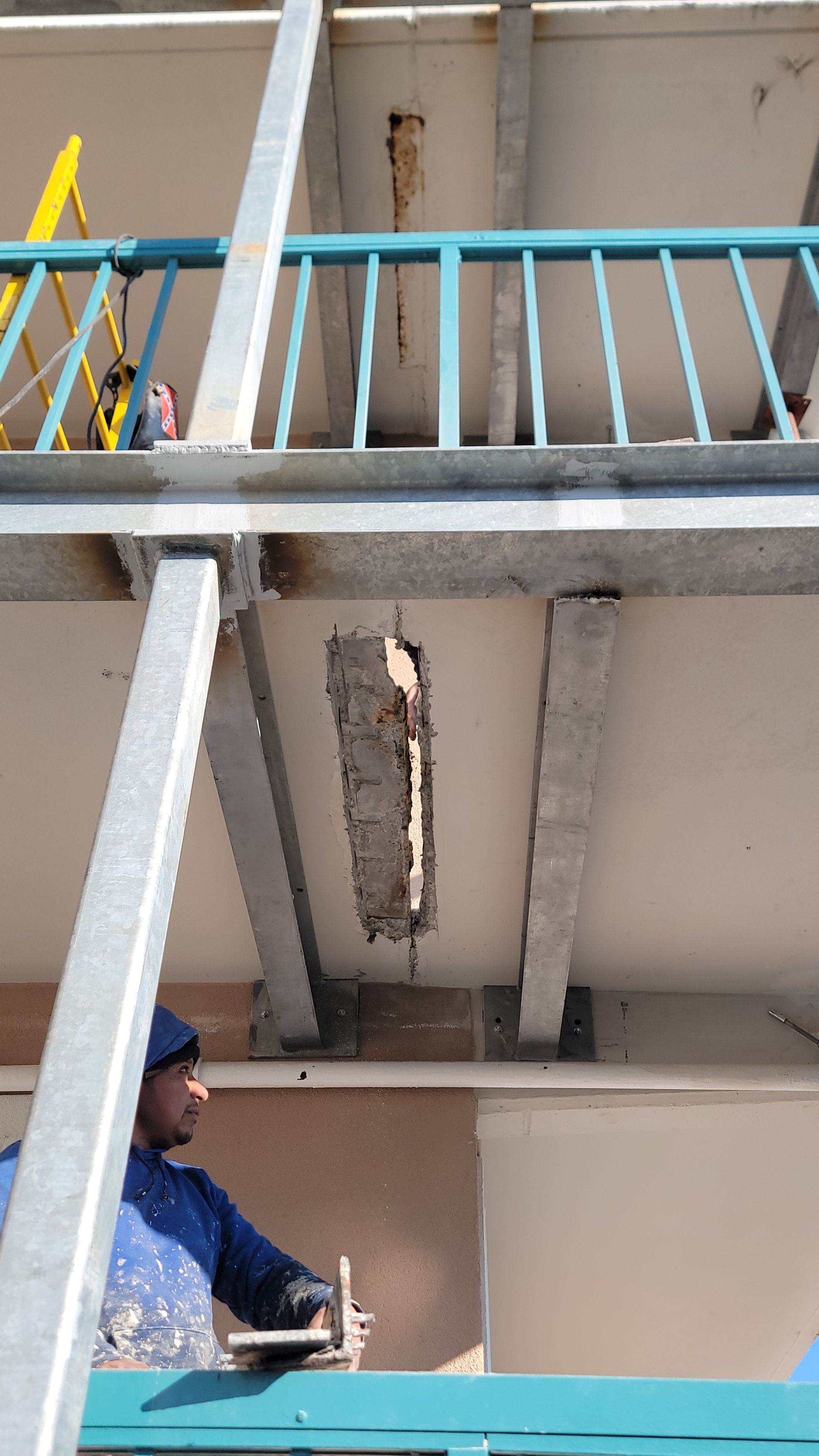 Man applying plaster to a damaged ceiling, with scaffolding and a balcony overhead.