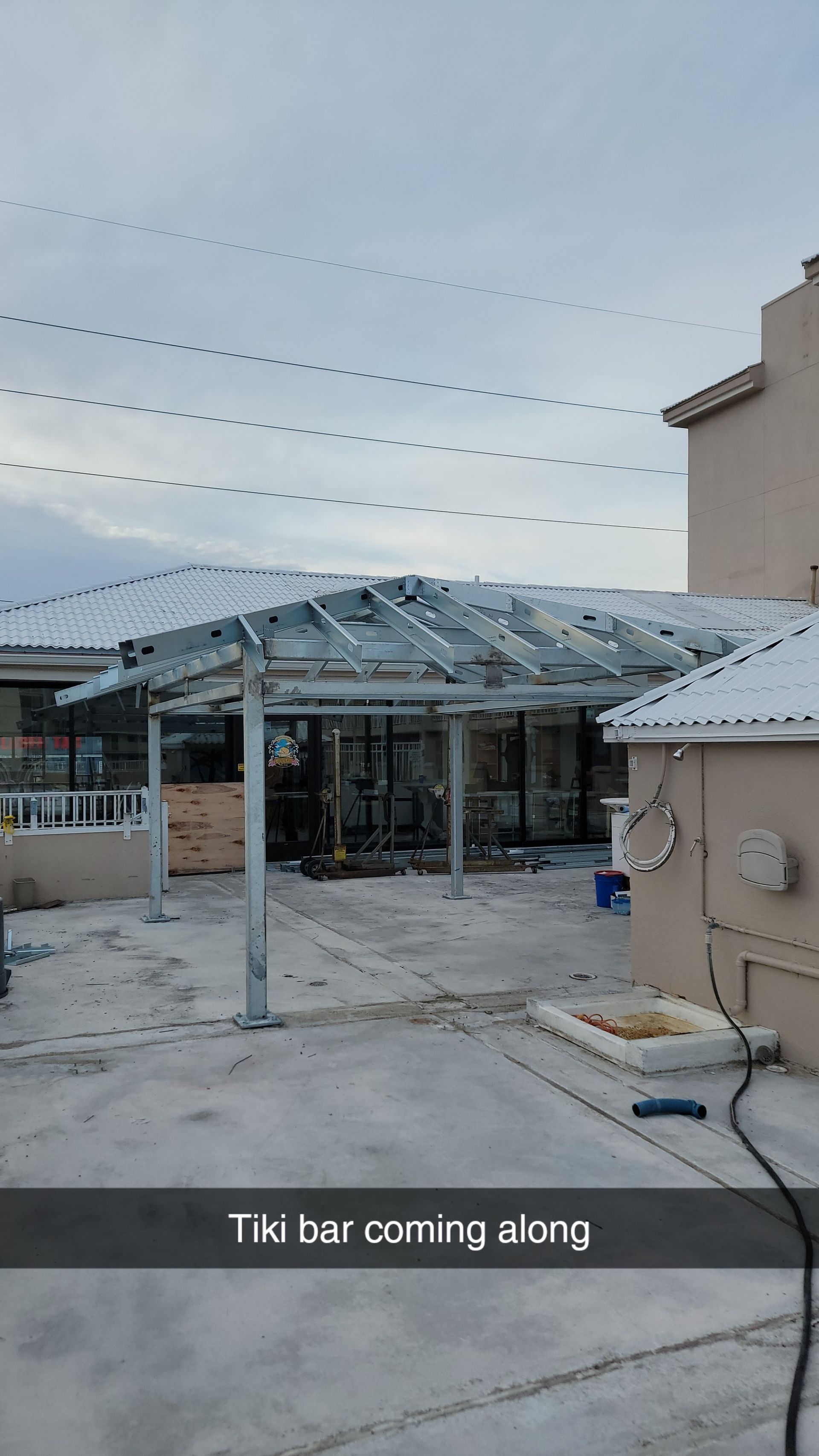 Metal frame of a tiki bar under construction in a paved outdoor area, with a house in the background.