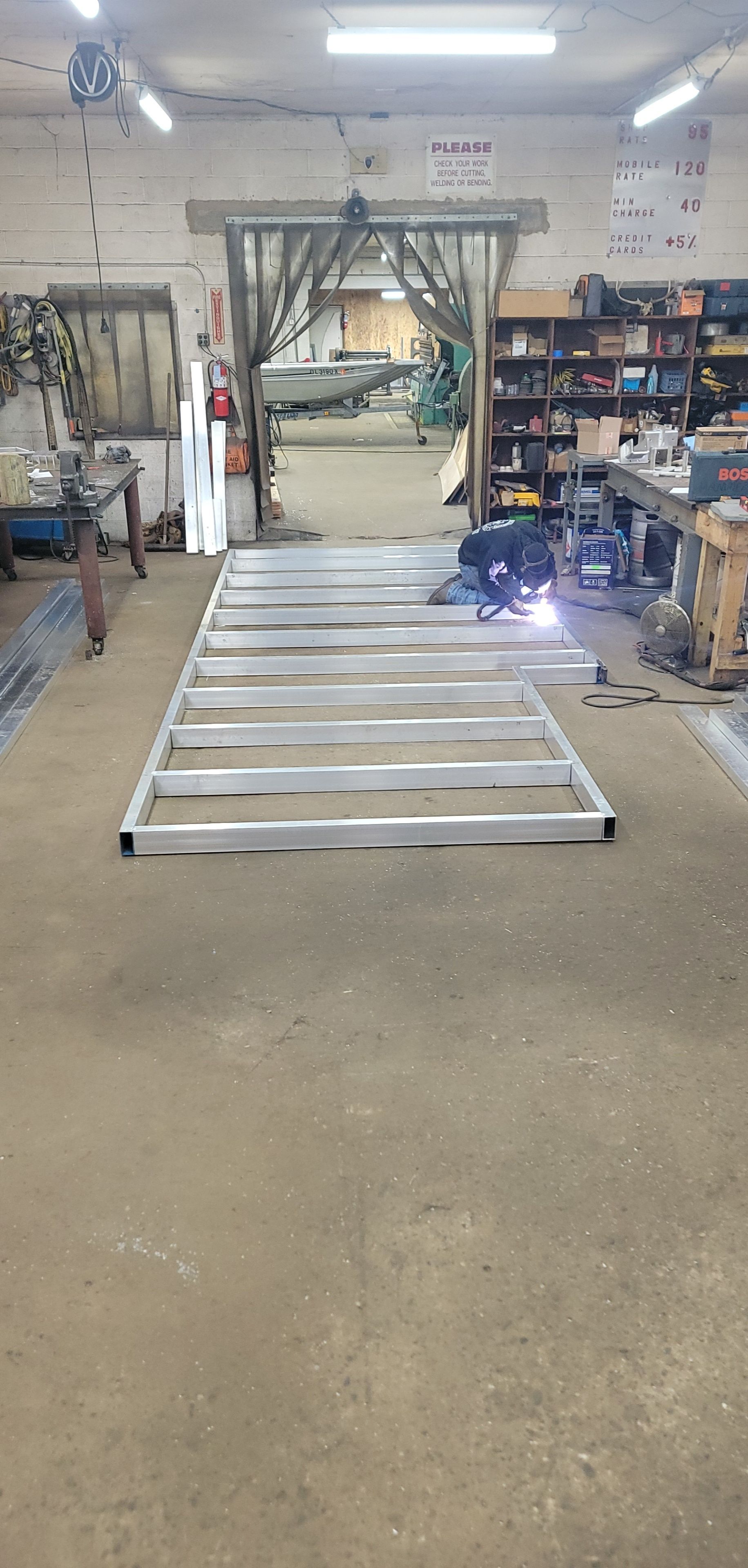 Welder working on a metal frame in a workshop. A door opens to a vehicle outside.