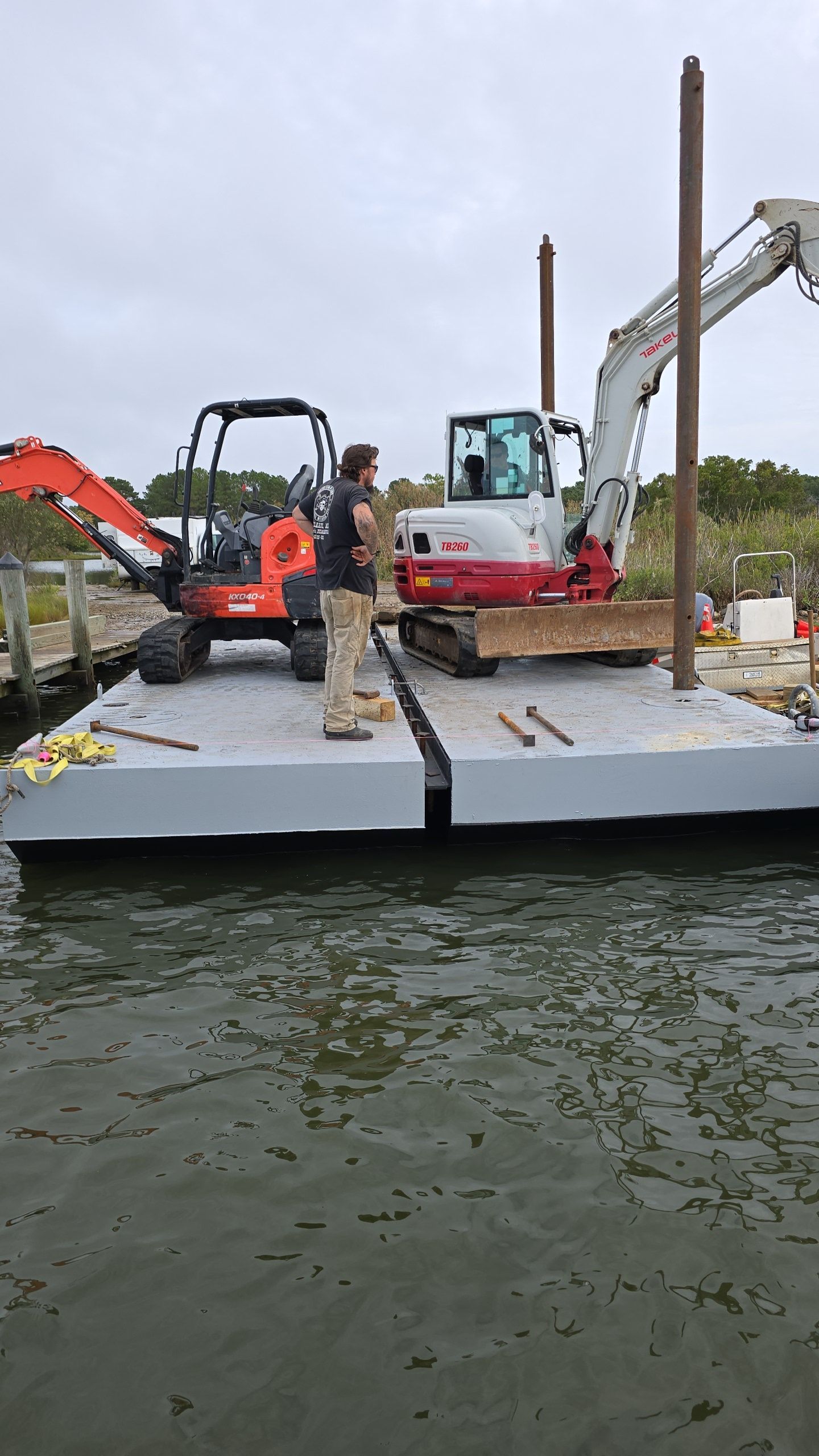 Construction site on water. Two excavators on a floating platform with a worker. Gray and white.