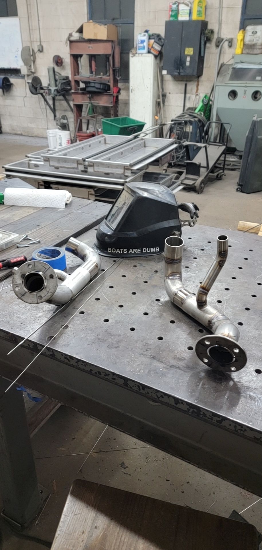 Welding shop scene with two metal pipes, welding mask, and work table.