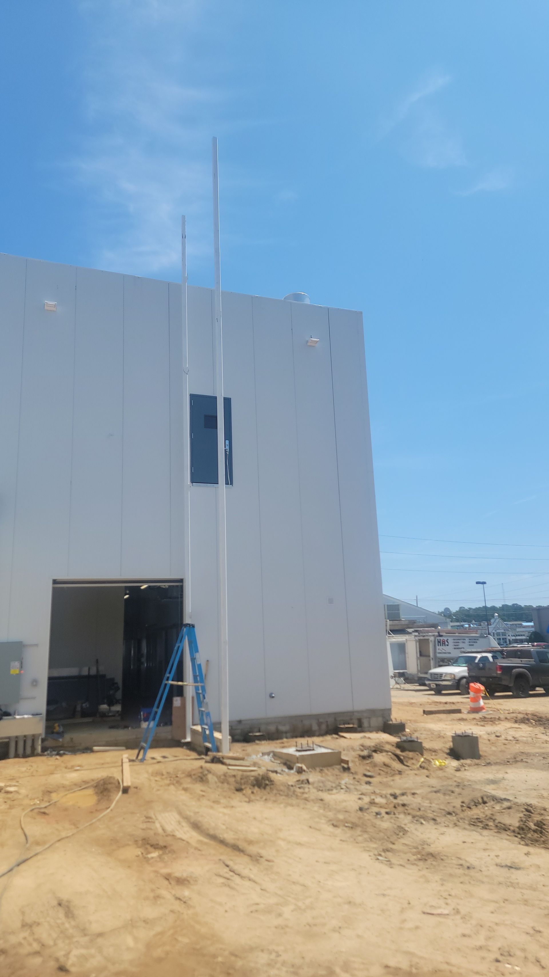 Construction site: white building with tall poles, blue sky, and dirt.