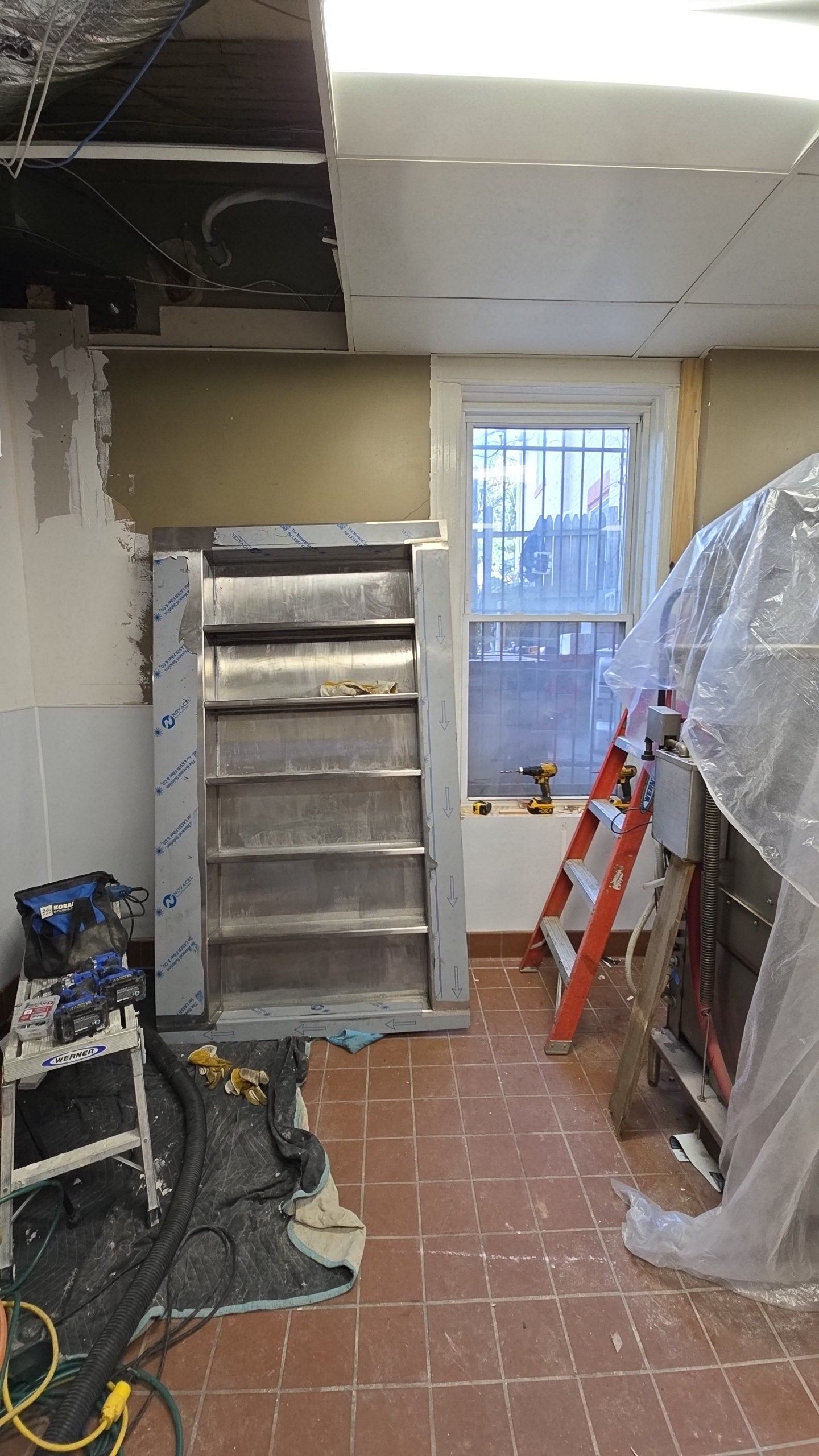 Restaurant interior under renovation with stainless steel shelving, window, ladder, and tools.
