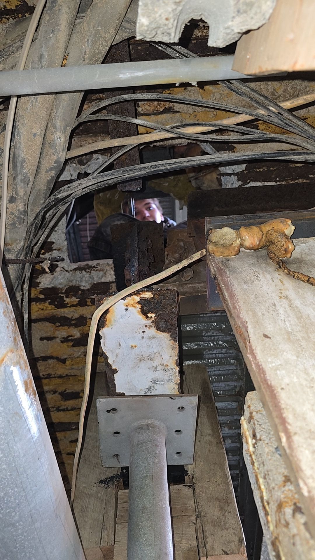 A person looking at rusted metal beams and support column under a structure.