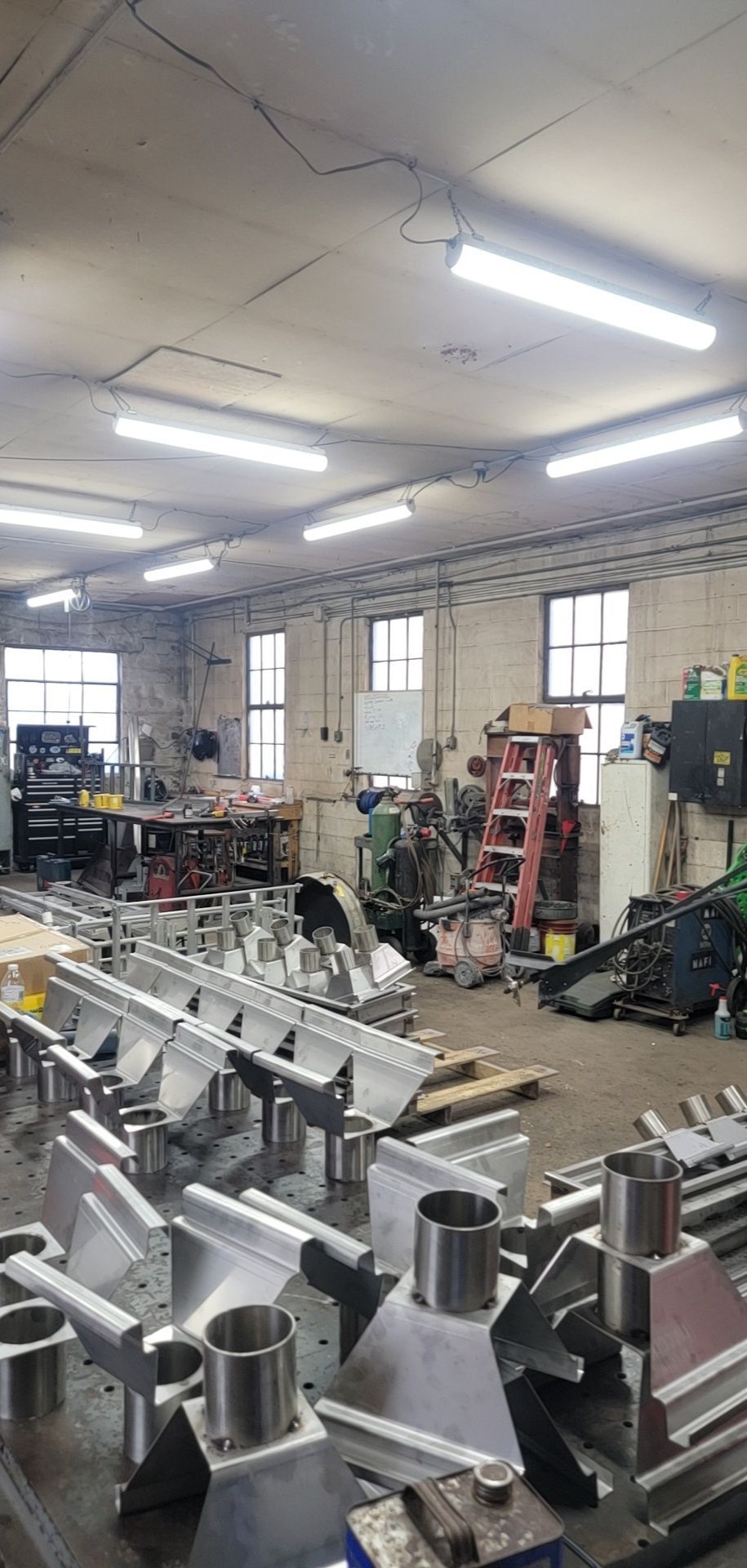 A workshop interior with metal equipment in the foreground and machinery and windows in the background.