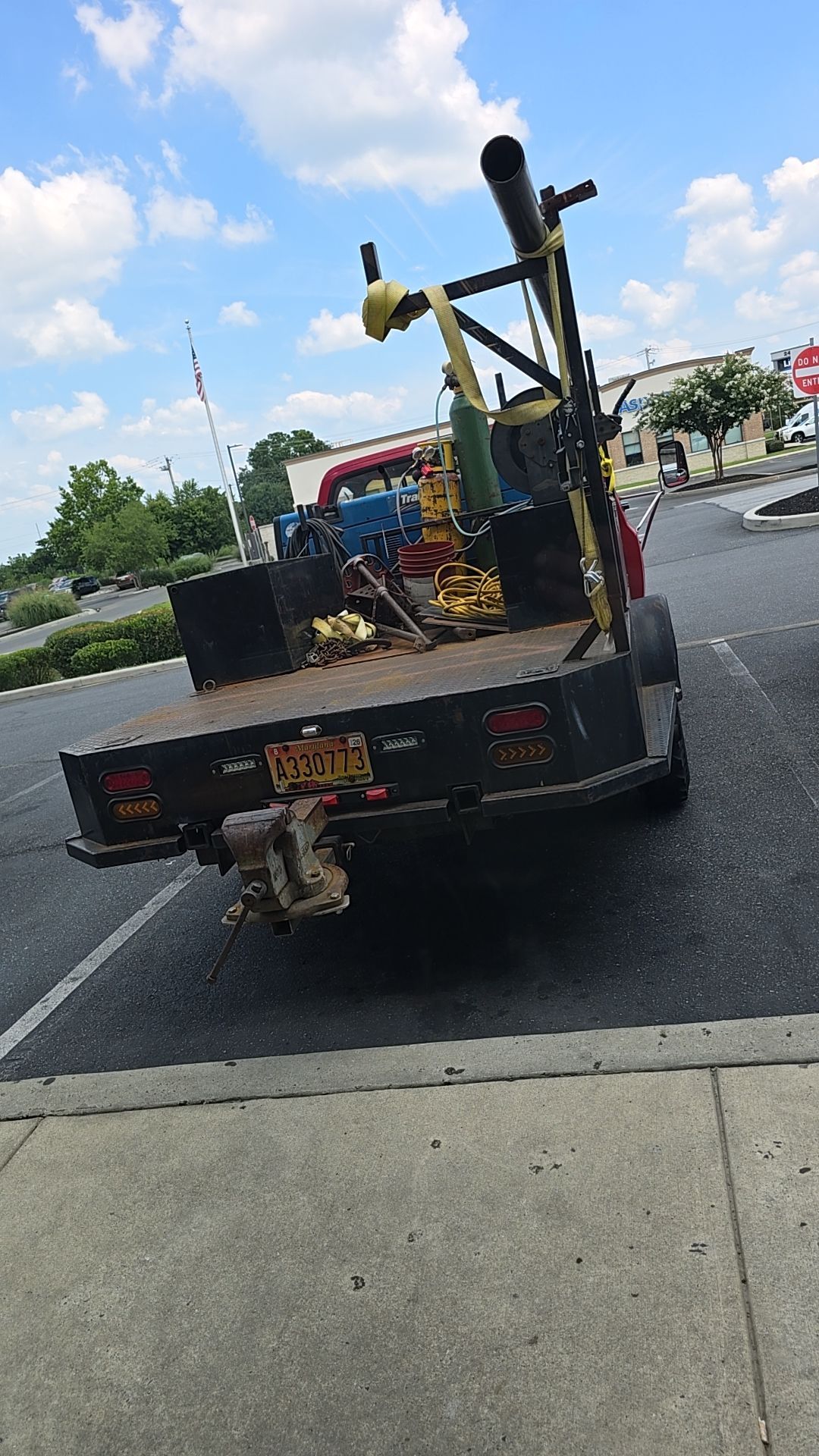 Red pickup truck with a flatbed, parked in a lot, loaded with equipment under a cloudy sky.