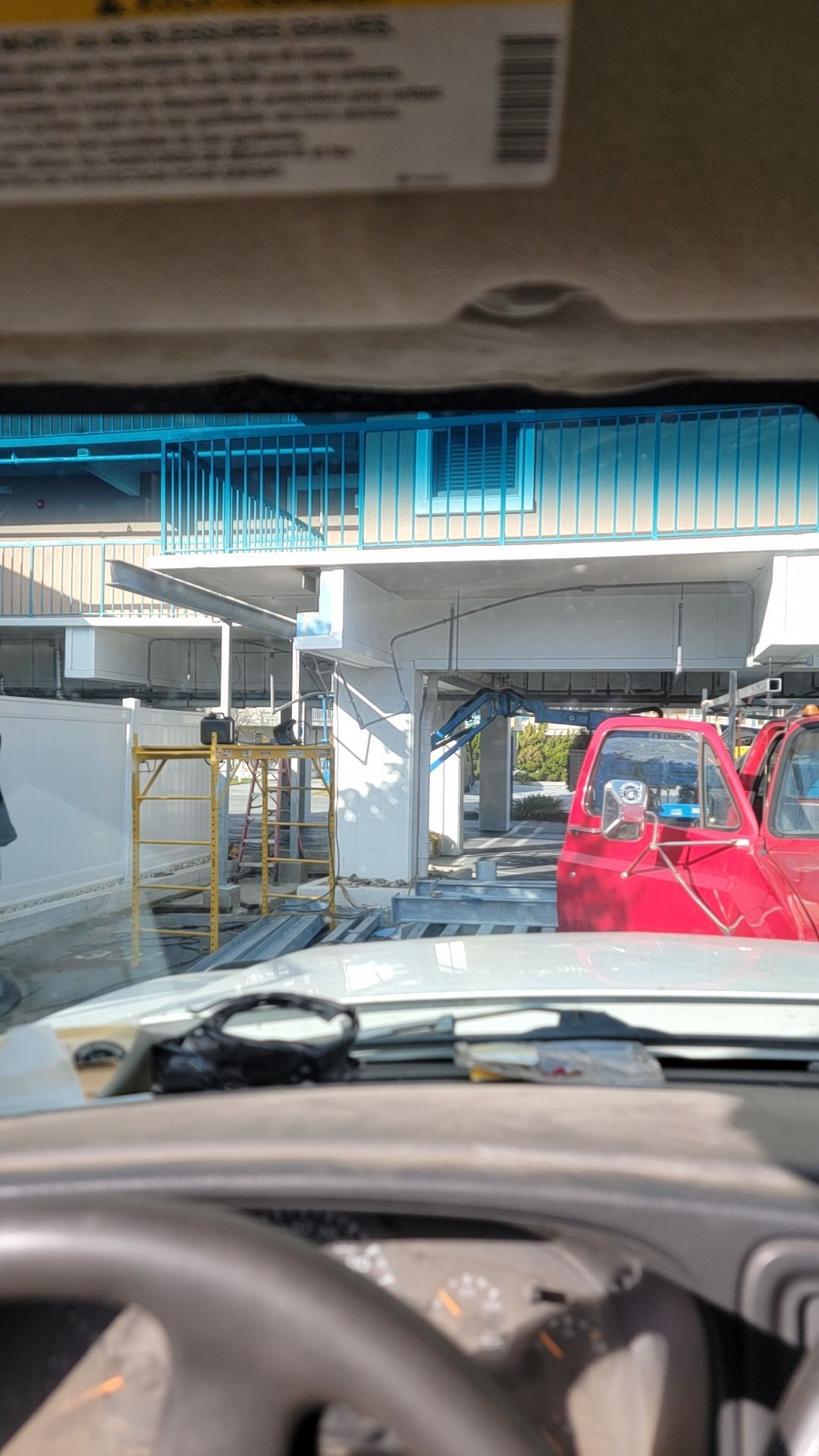 View from a car's dashboard. A red truck is parked near a concrete structure. Sun visor is down.