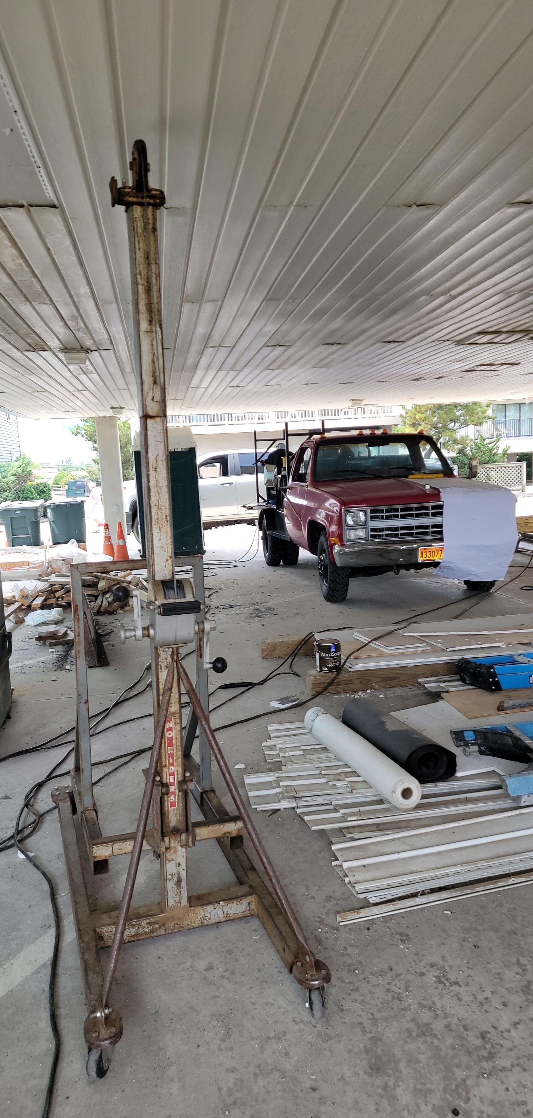 Rusty construction lift under a white canopy with a red pickup truck.