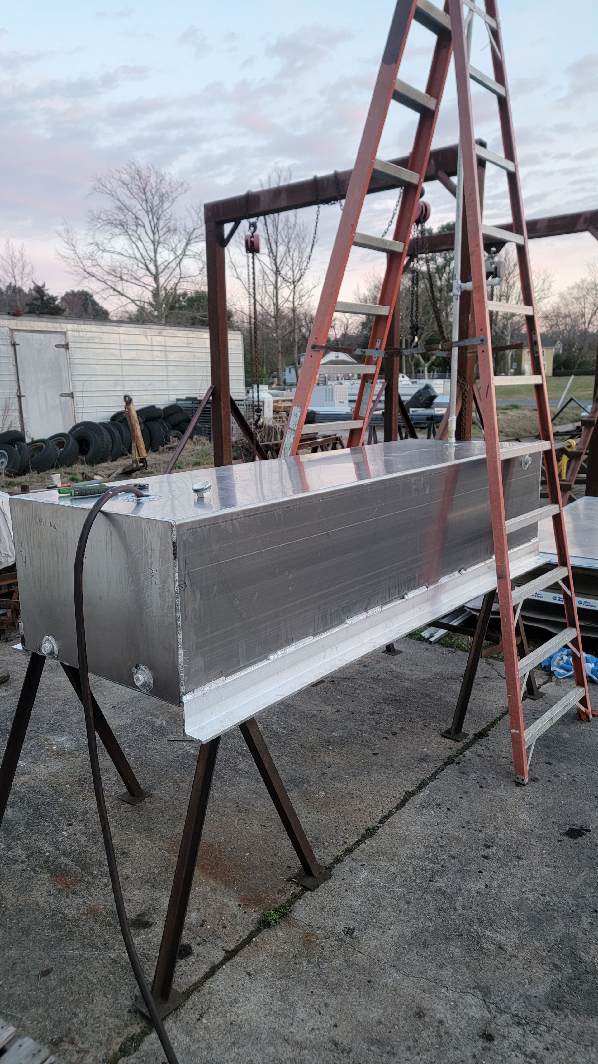 Long metal trough on sawhorses, next to a ladder outdoors.