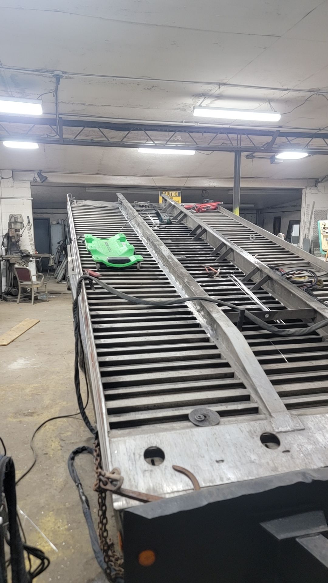Metal truck trailer with ramp inside a garage. Green object sits on the ramp.