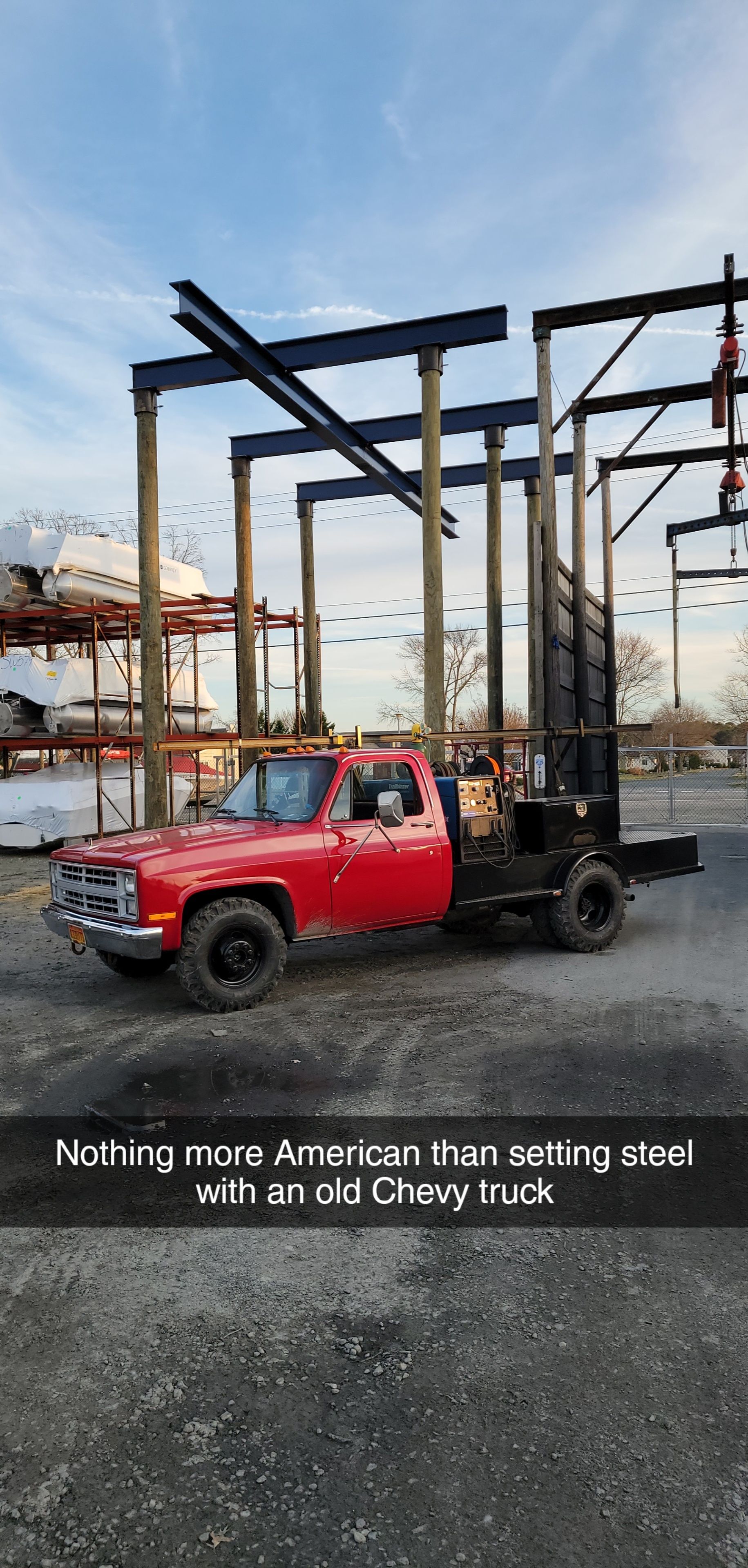 Red Chevy truck parked under steel beams at a construction site.