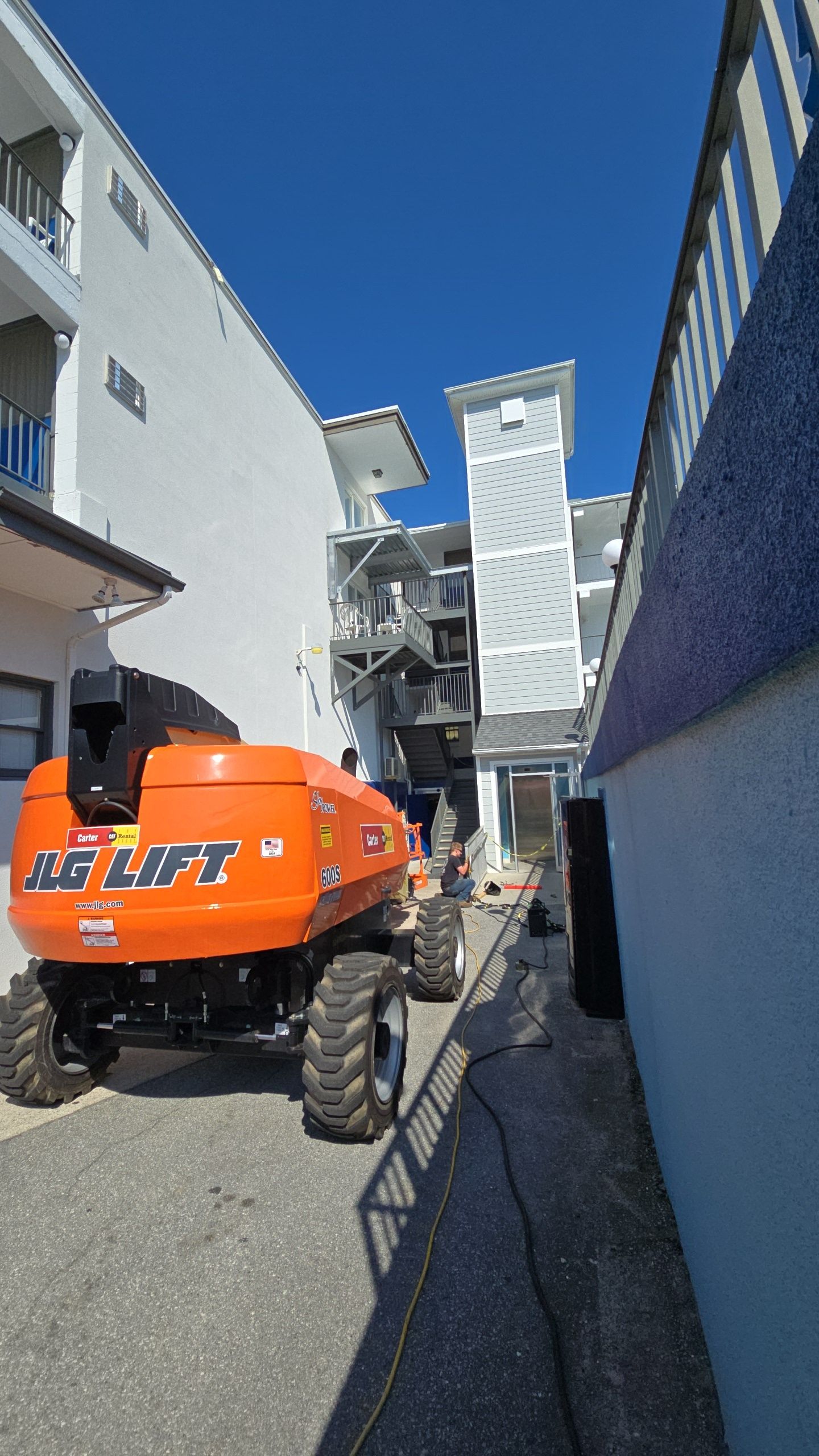 Orange AB Lift vehicle in a narrow alleyway between white buildings on a sunny day.