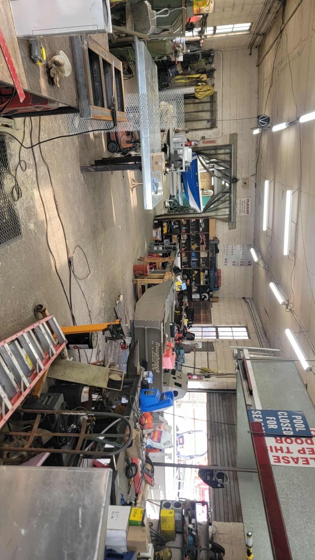 Workshop interior, equipment and tools. Grey walls, overhead lighting, various machinery, and a ladder.